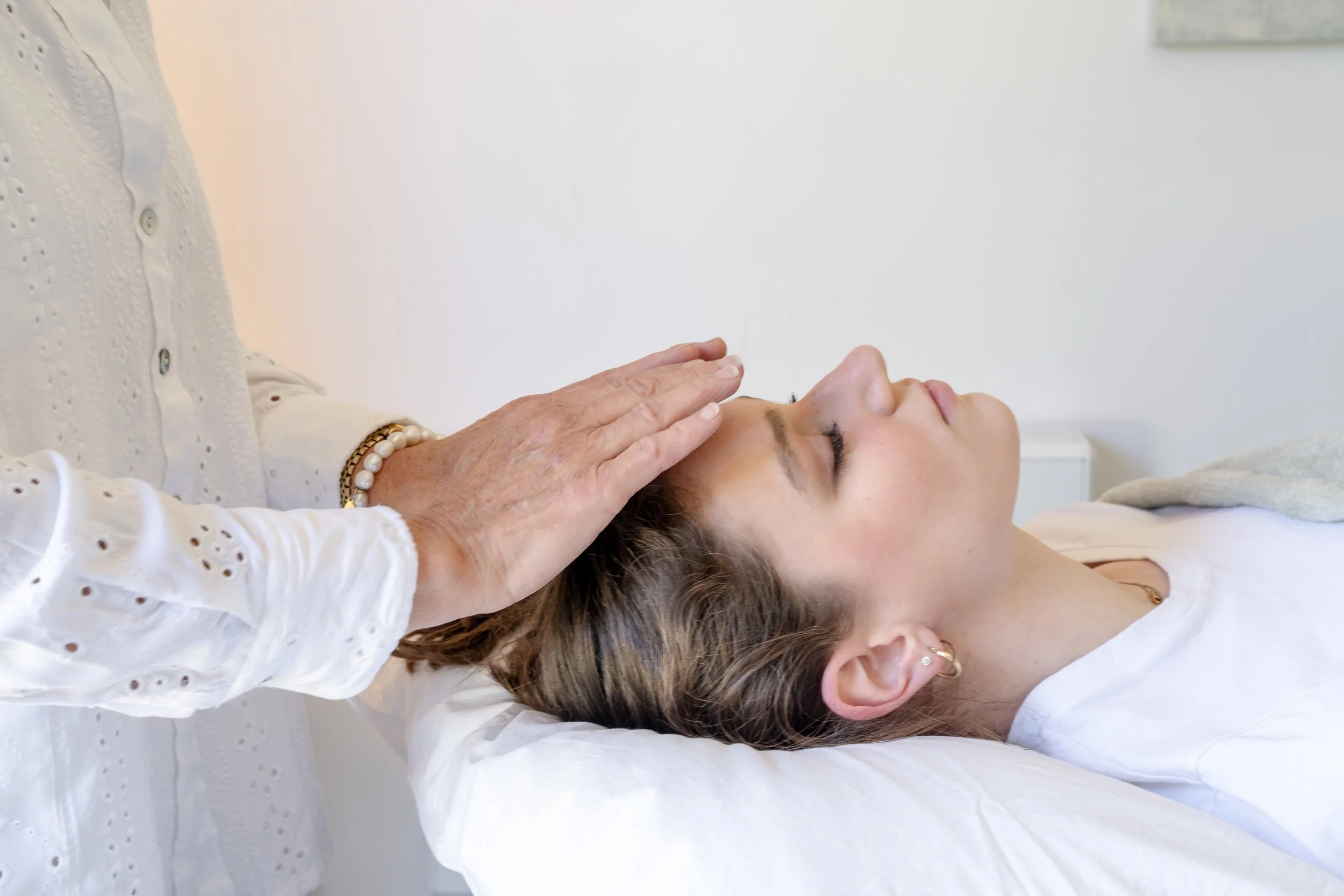 Woman lying on a treatment bed with eyes closed, receiving a Reiki from a therapist.