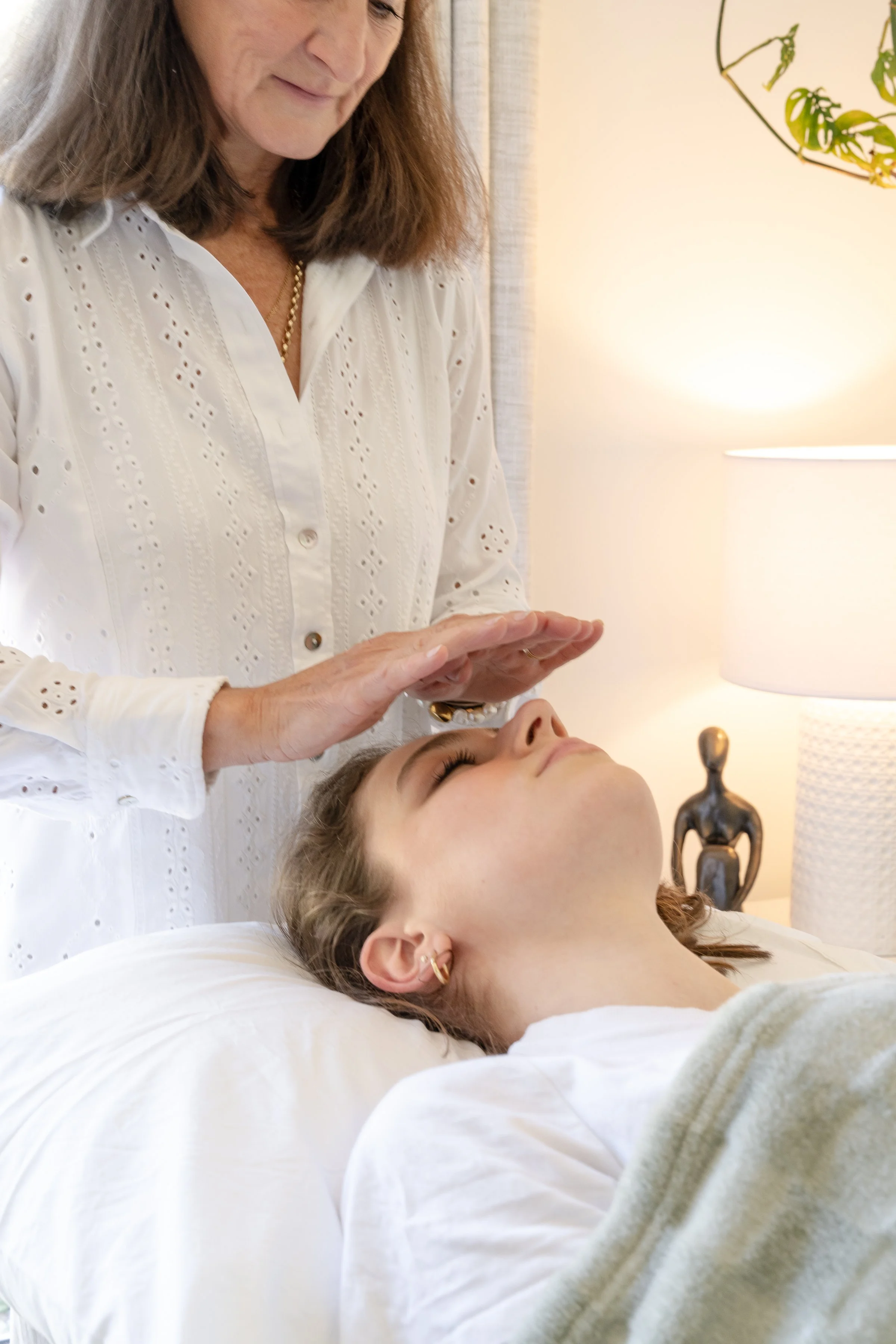 lady performing reiki on young lady. Hands hovering over lady laying down.