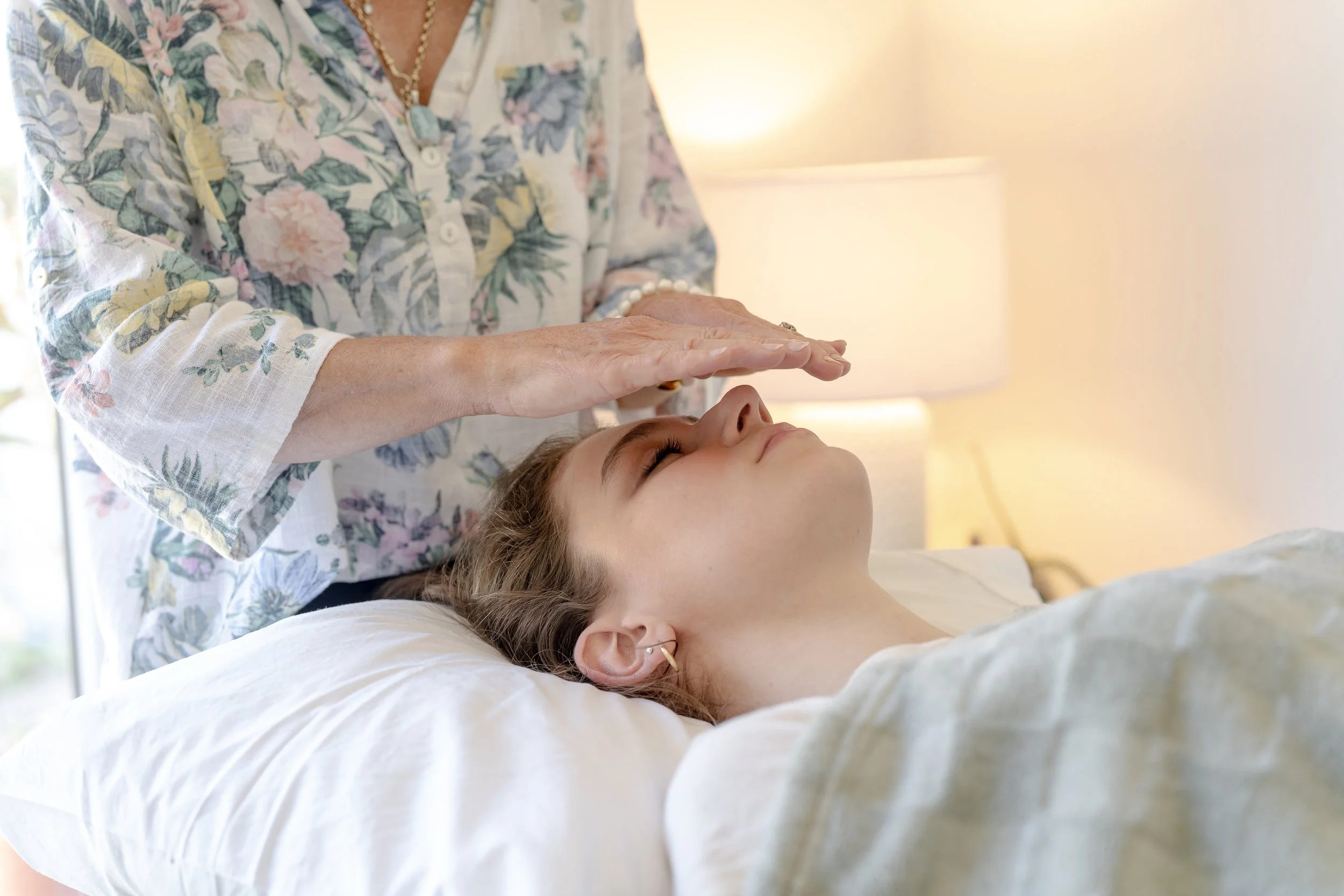lady in floral shirt performing reiki on client. She is hovering her hands over the clients face.