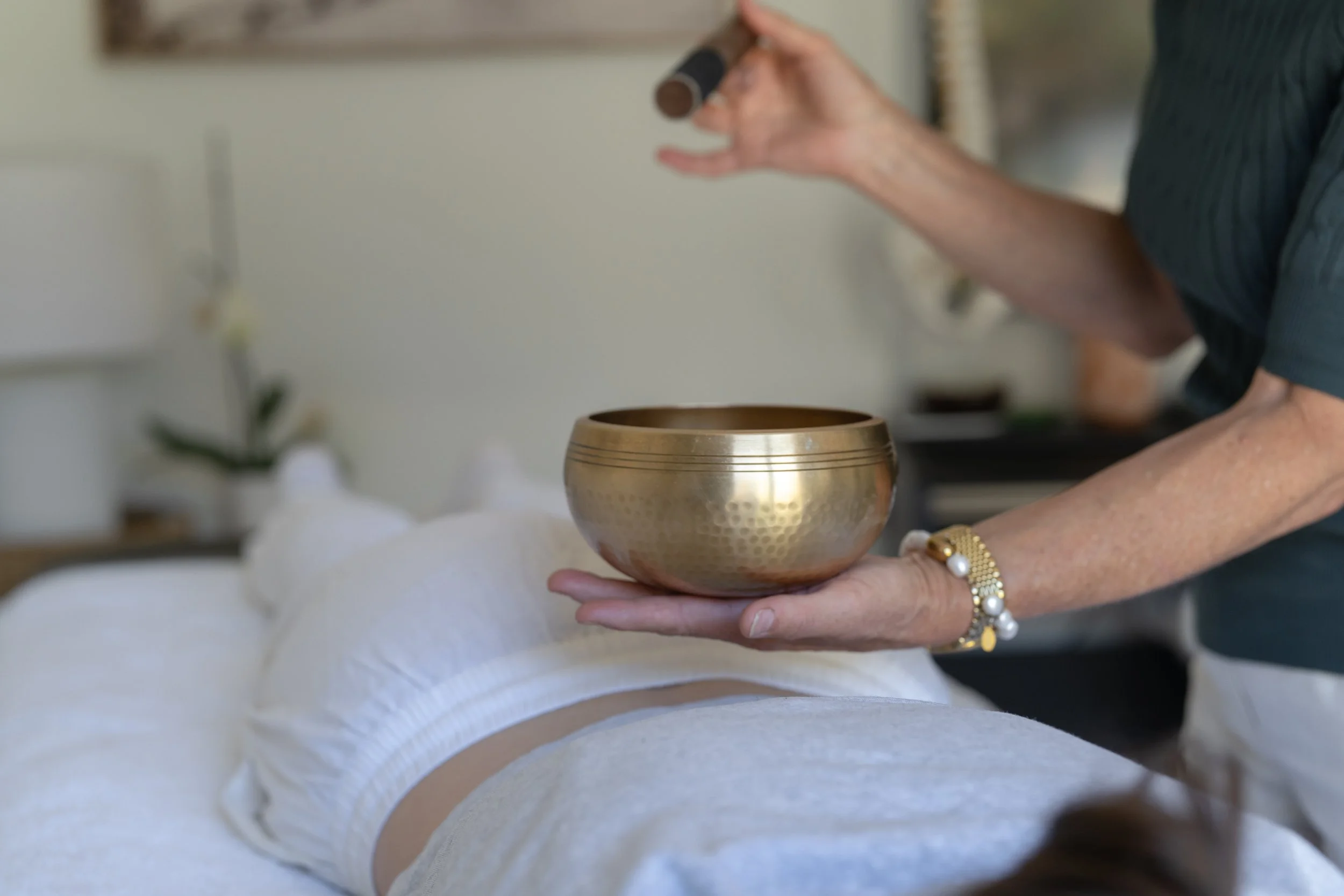Person holding a singing bowl in one hand while playing a mallet with the other hand during a sound healing session