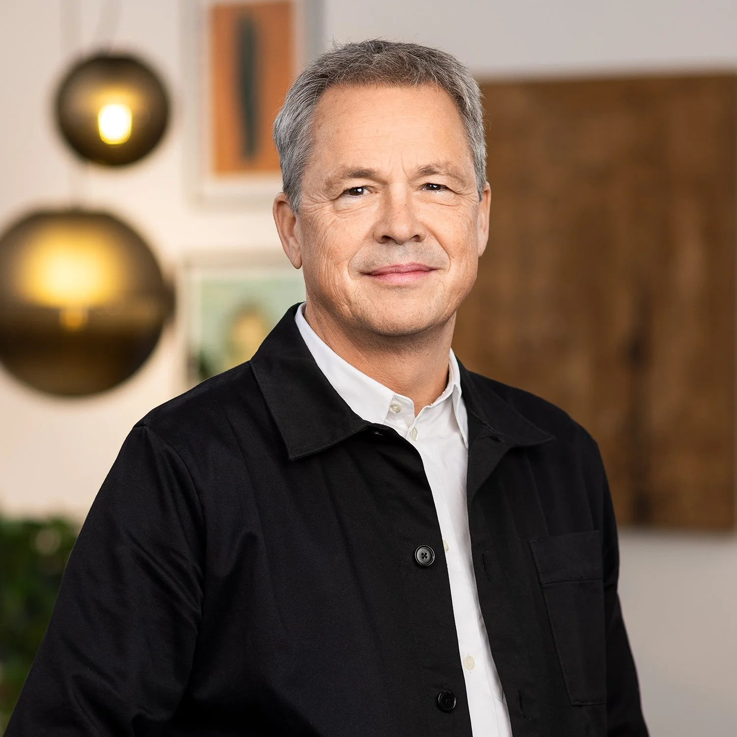A middle-aged man with gray hair wearing a black jacket over a white collared shirt, smiling slightly.