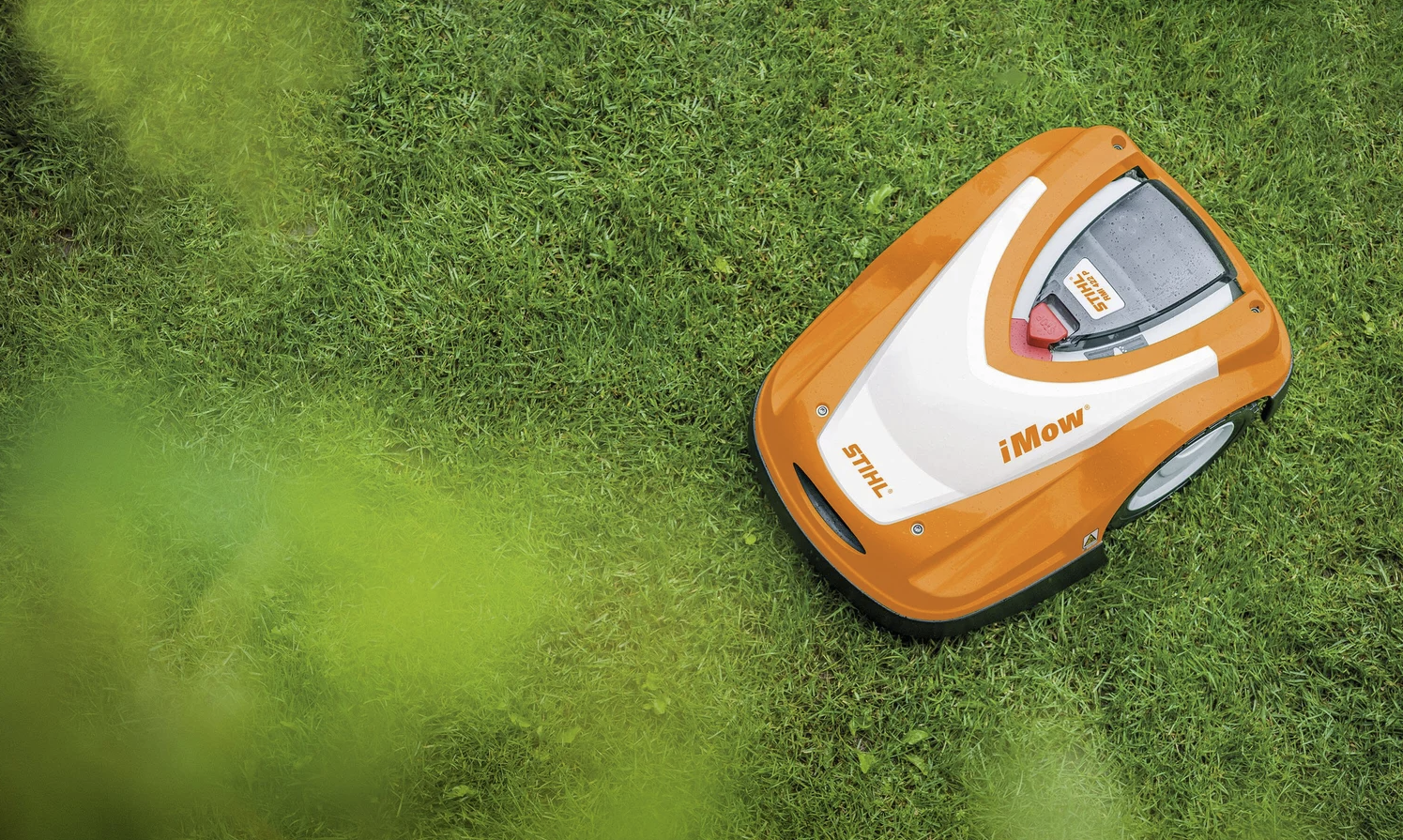 An orange and white robotic lawn mower on a green grassy lawn.
