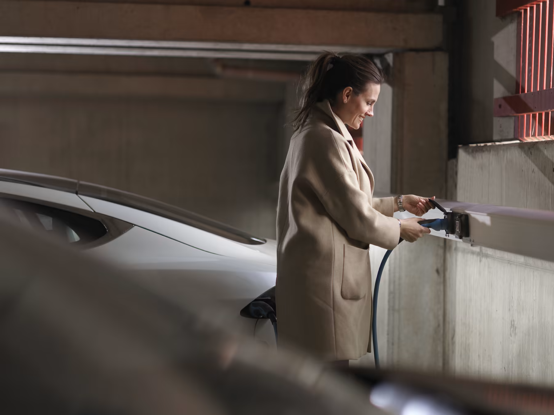Woman charging a silver electric car in an underground parking garage.