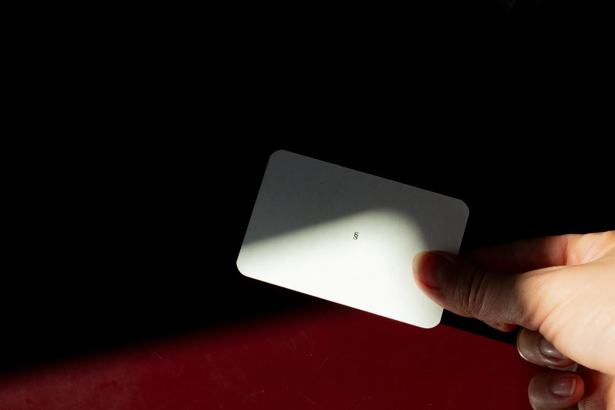 Notár drží podpisový doklad alebo kartu počas overovania dokumentu, čiastočne osvetlený na tmavom pozadí.