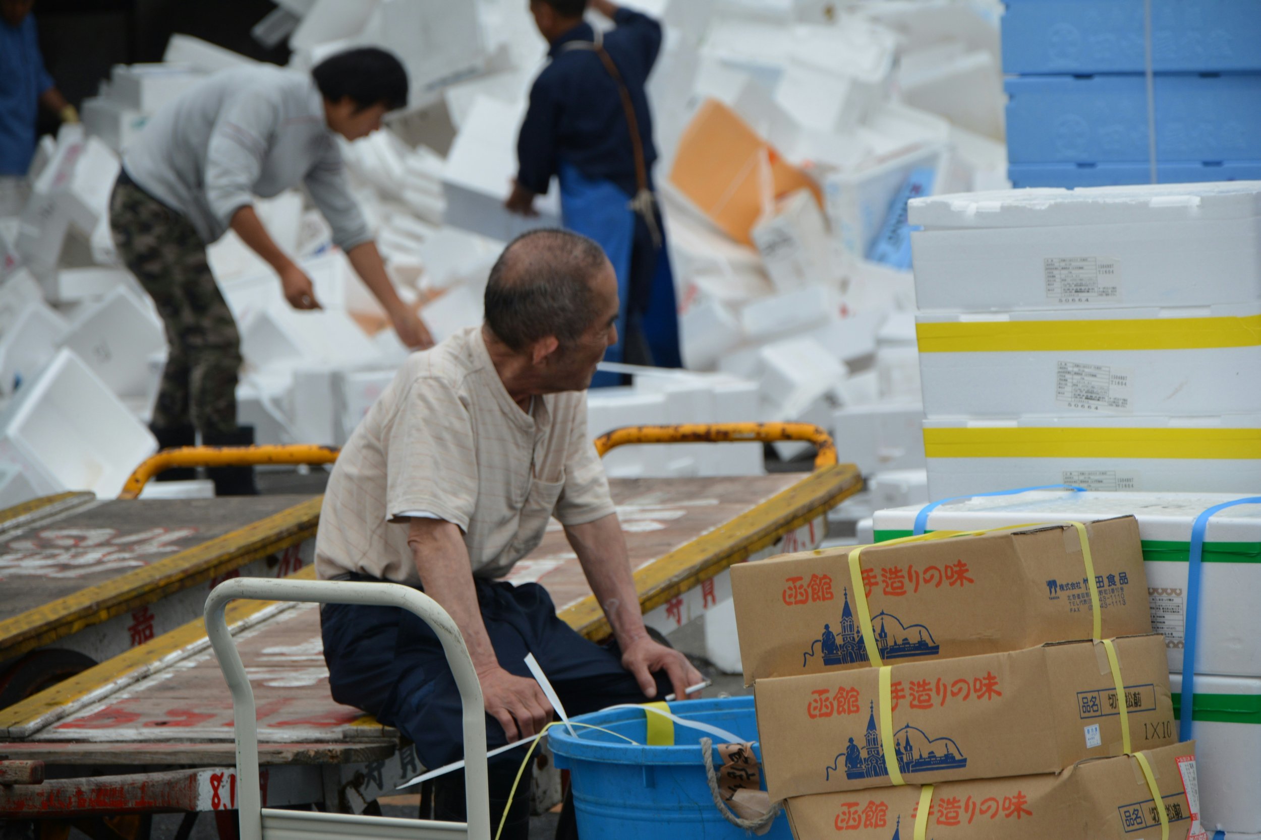 People sorting and organizing cardboard boxes and styrofoam containers in what appears to be a warehouse or sorting facility.