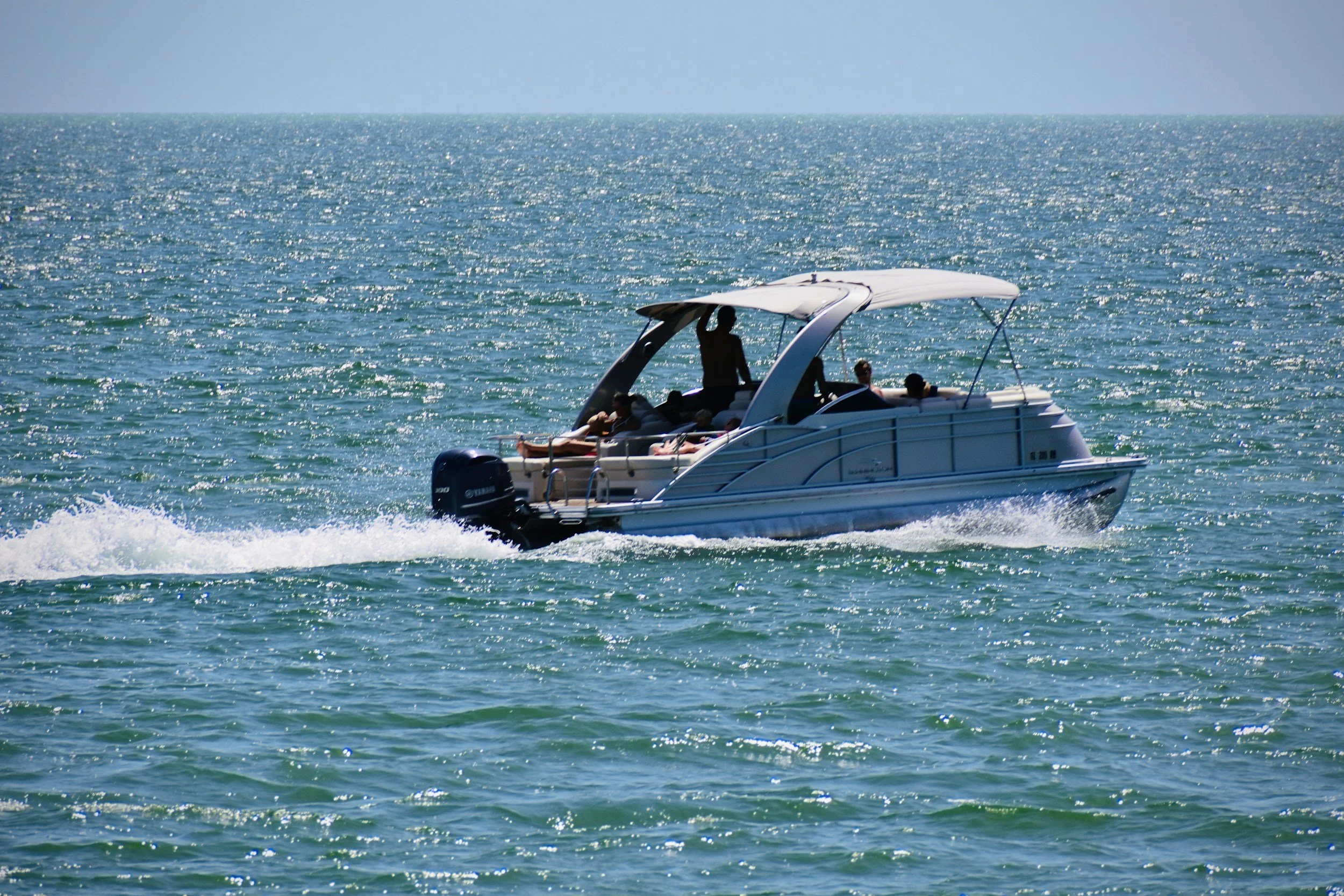 A speedboat on the ocean with three people onboard and a person standing and waving.