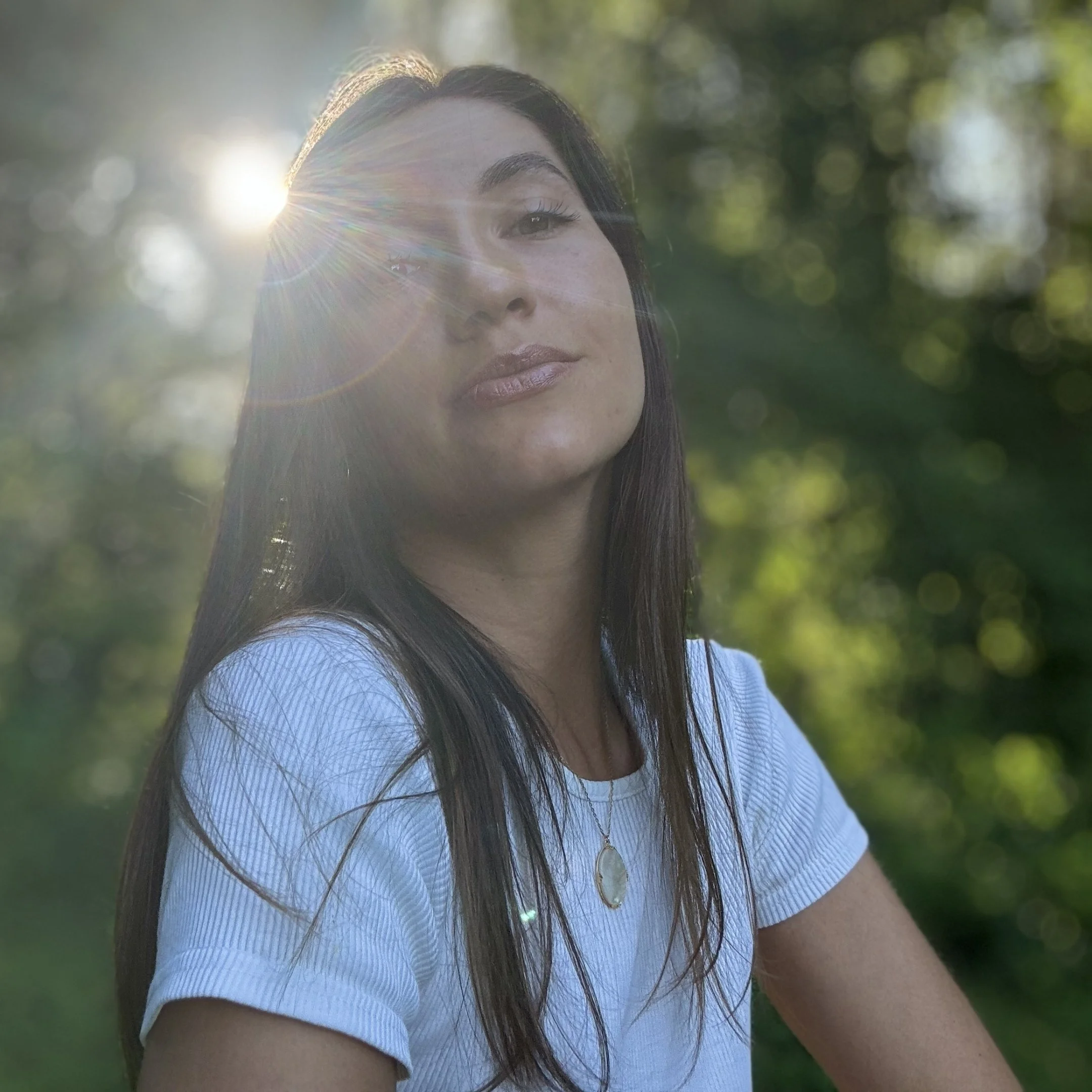 Sarah Gandon avec des cheveux longs et une chemise blanche, souriante, avec le soleil à l'arrière-plan.