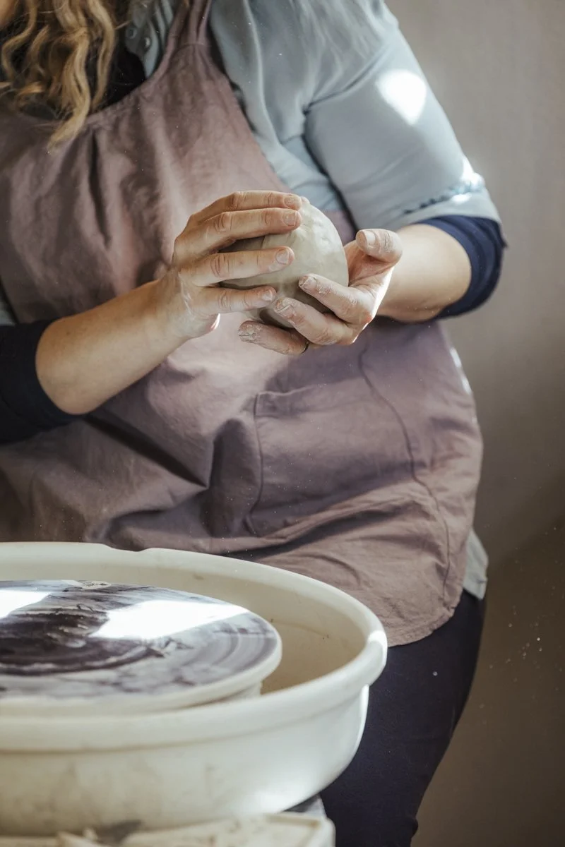Hände halten eine Tonkugel vor einer Drehscheibe