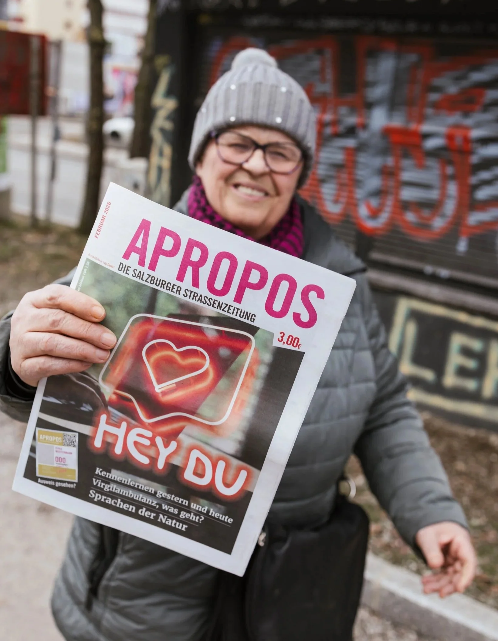 Frau hält lächelnd Straßenzeitung in die Kamera