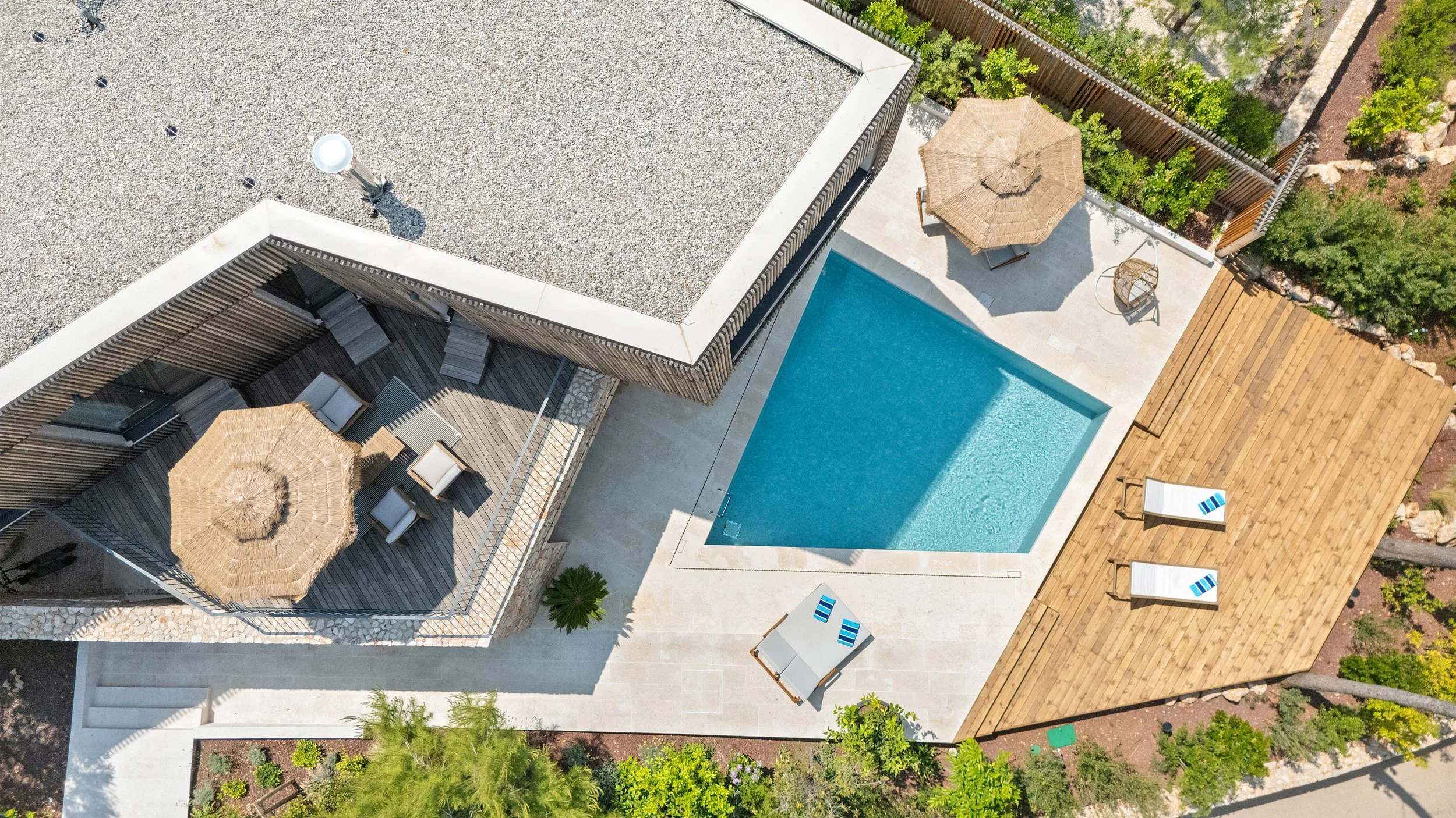 Aerial view of a backyard with a swimming pool, sun loungers, umbrellas, patio furniture, and surrounding greenery.