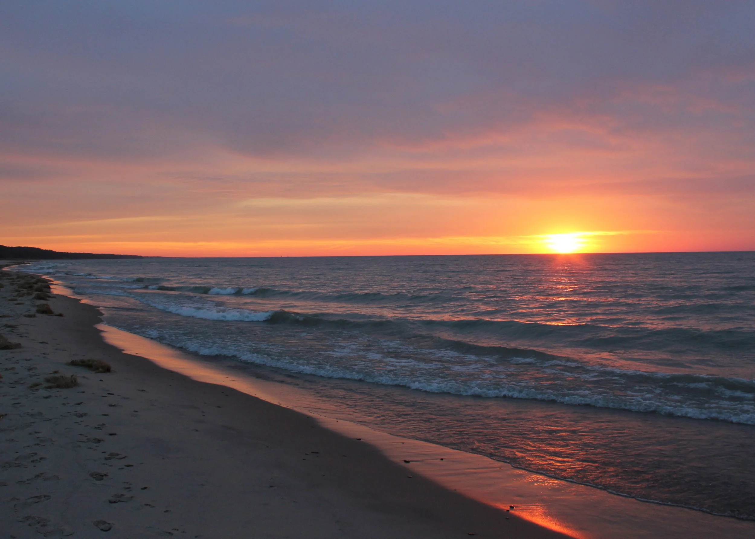 Sunset over the ocean with colorful sky, gentle waves on the sandy beach.