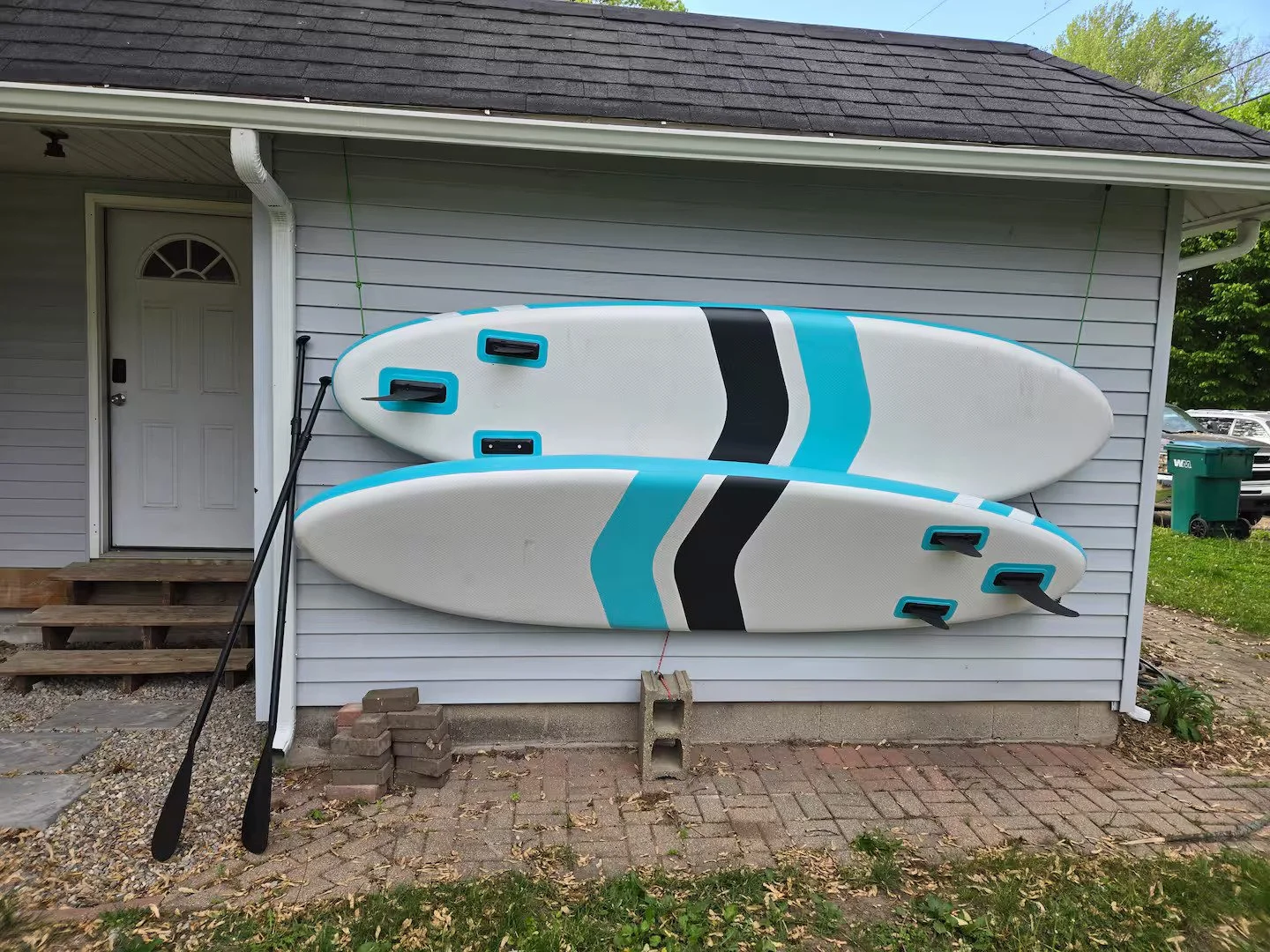 Two paddleboards are mounted on the exterior wall of a house with gray siding.