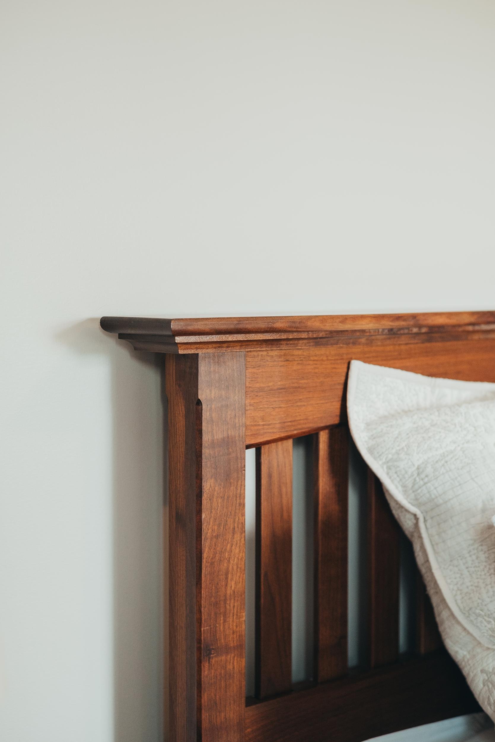 Close-up of a wooden bed frame with a partial view of a quilted white pillow.