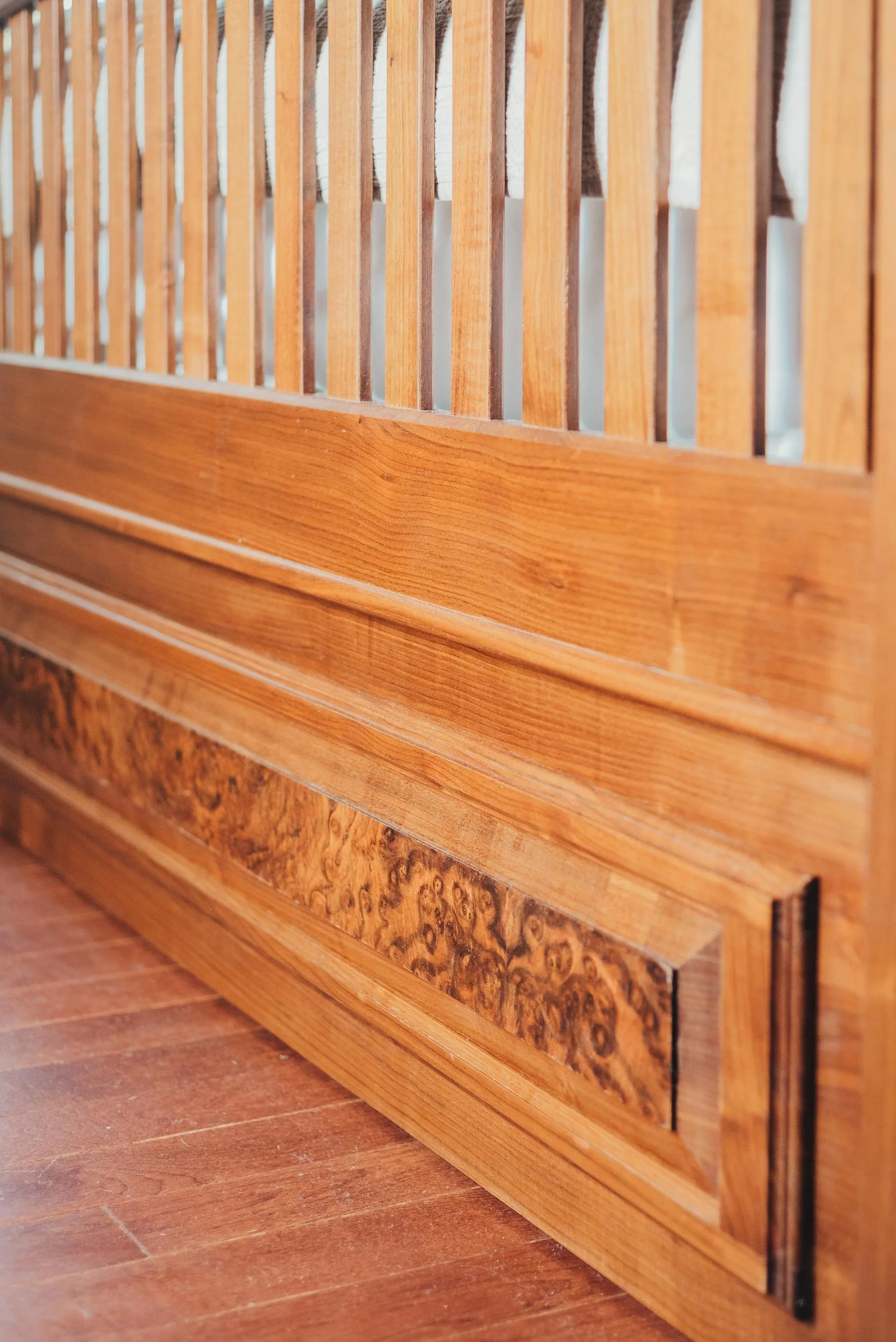 Close-up of a wooden bed frame with horizontal slats and a decorative bottom panel, on a hardwood floor.