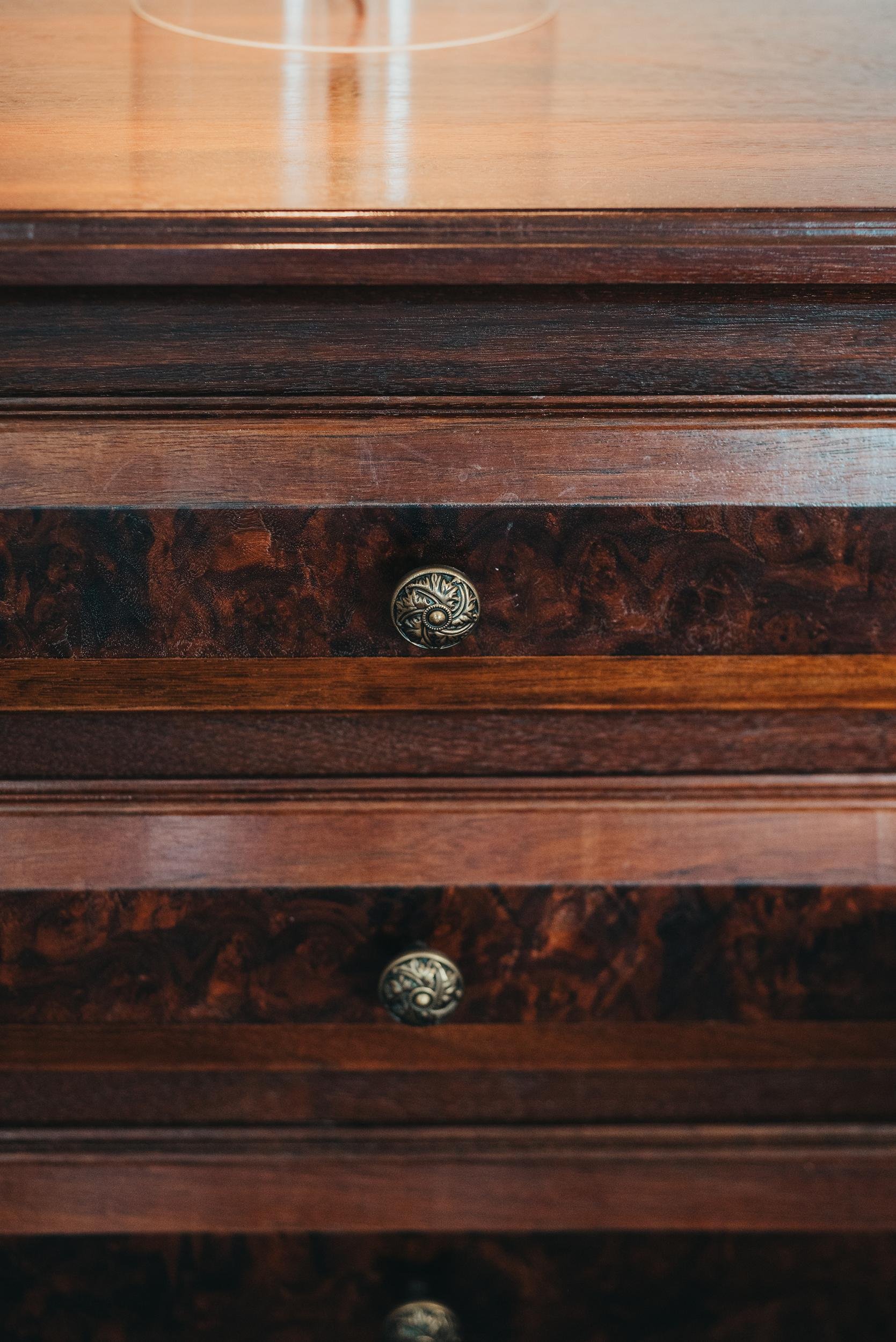 Close-up of a wooden dresser with ornate round metal knobs on the drawers.