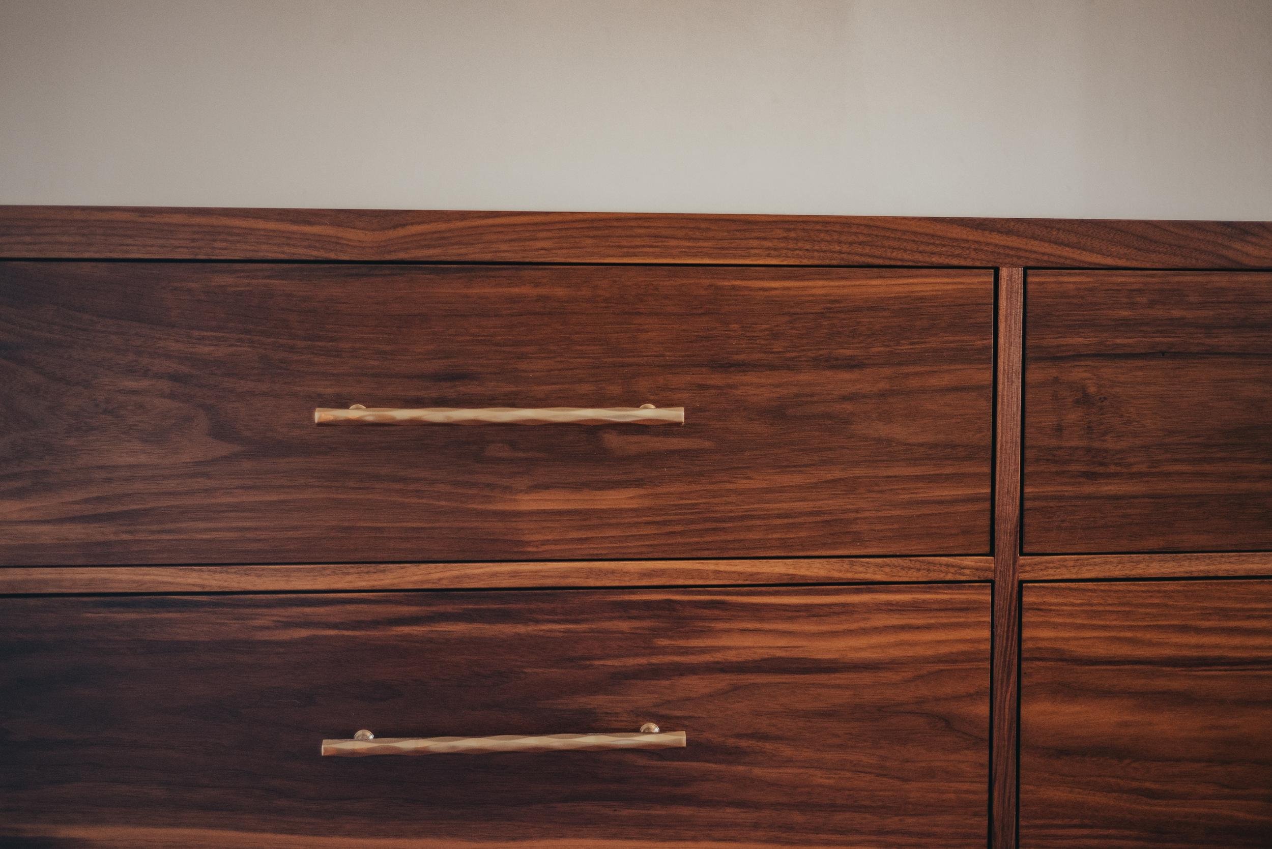 Close-up of a wooden dresser with horizontal drawers and light-colored handles against a white wall.