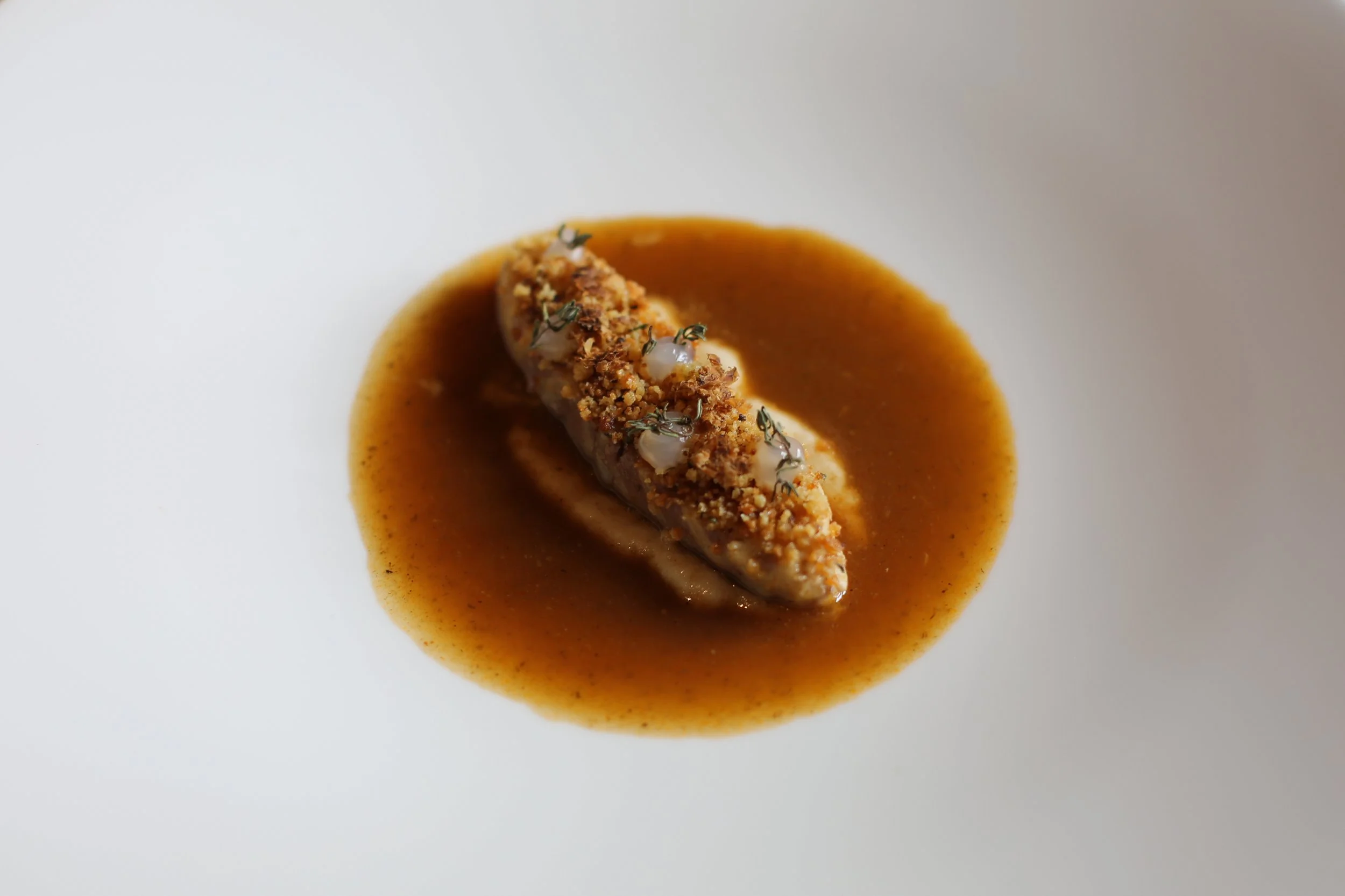 Feines Gericht mit einer gefüllten Rolle in brauner Soße, garniert mit Kräutern und gehackten Nüssen.