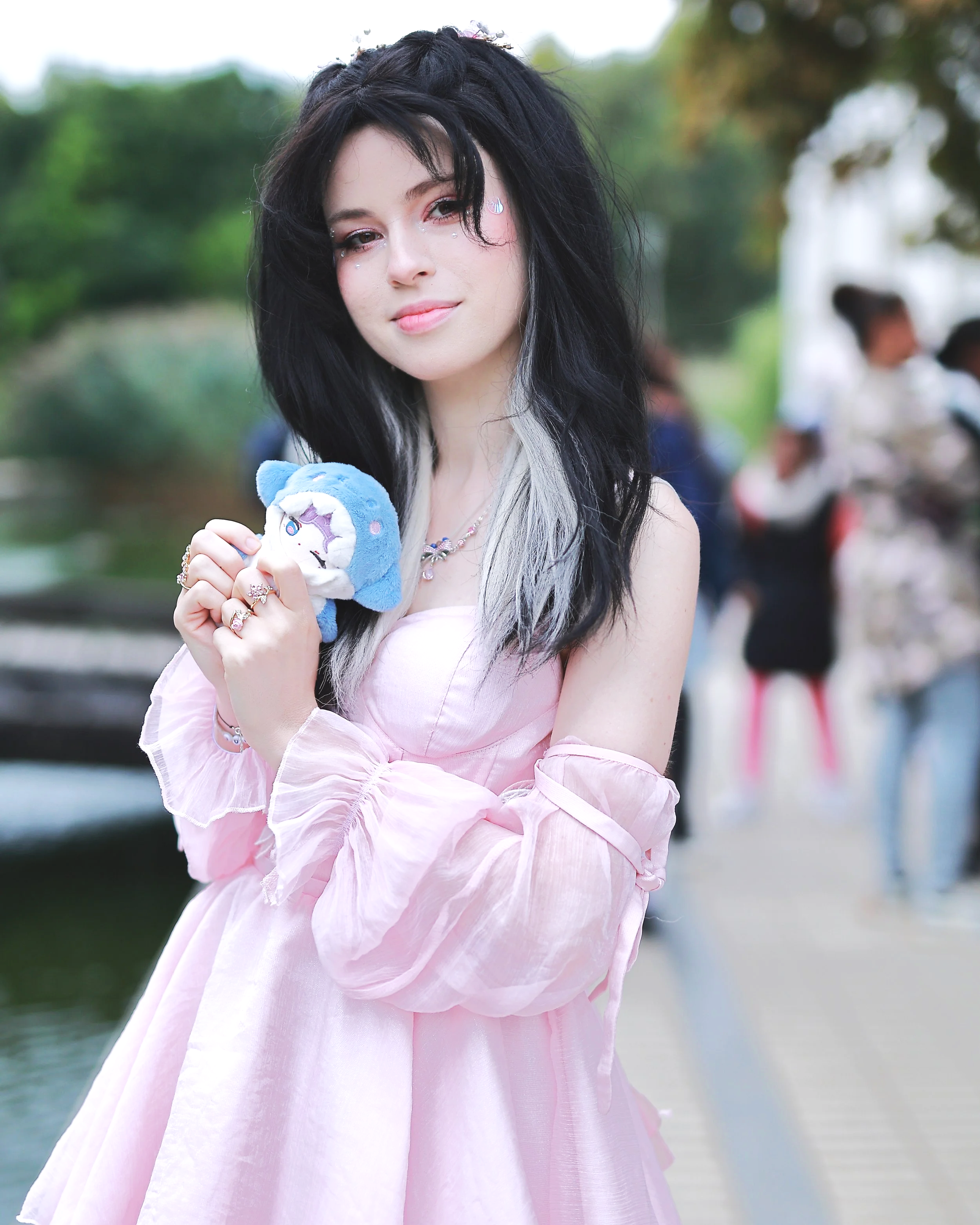 Young woman with black and white hair holding a plush toy in a pink dress outdoors. cosplayer cosplay portrait anime manga gaming