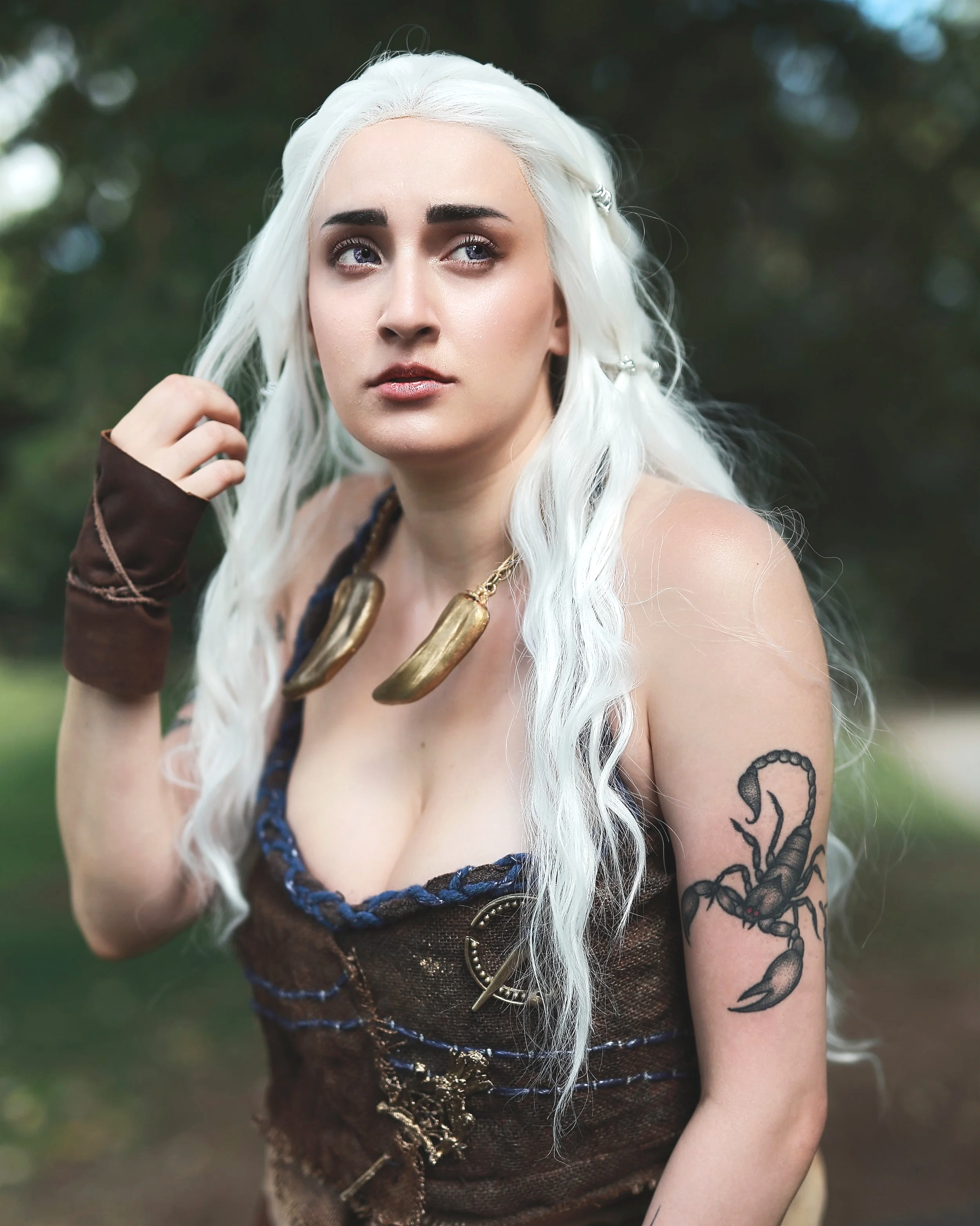 Woman with long white hair, scorpion tattoo on shoulder, dressed in pirate-themed outfit with necklace and arm guard, standing outdoors. Daenerys Game of thrones cosplay cosplayer