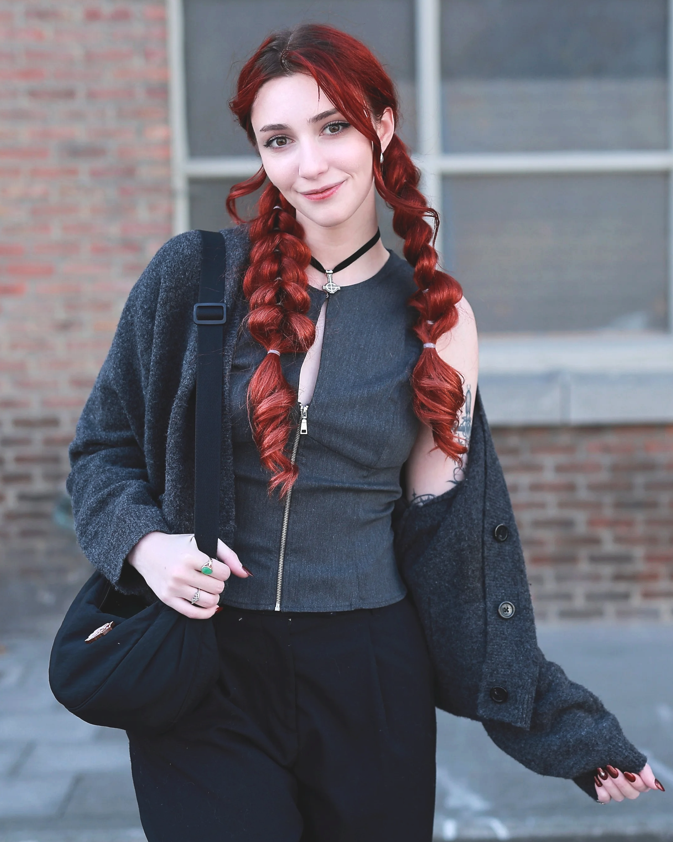 Une jeune femme avec cheveux roux tressés souriante se tient devant un bâtiment en brique portrait beauté fashion