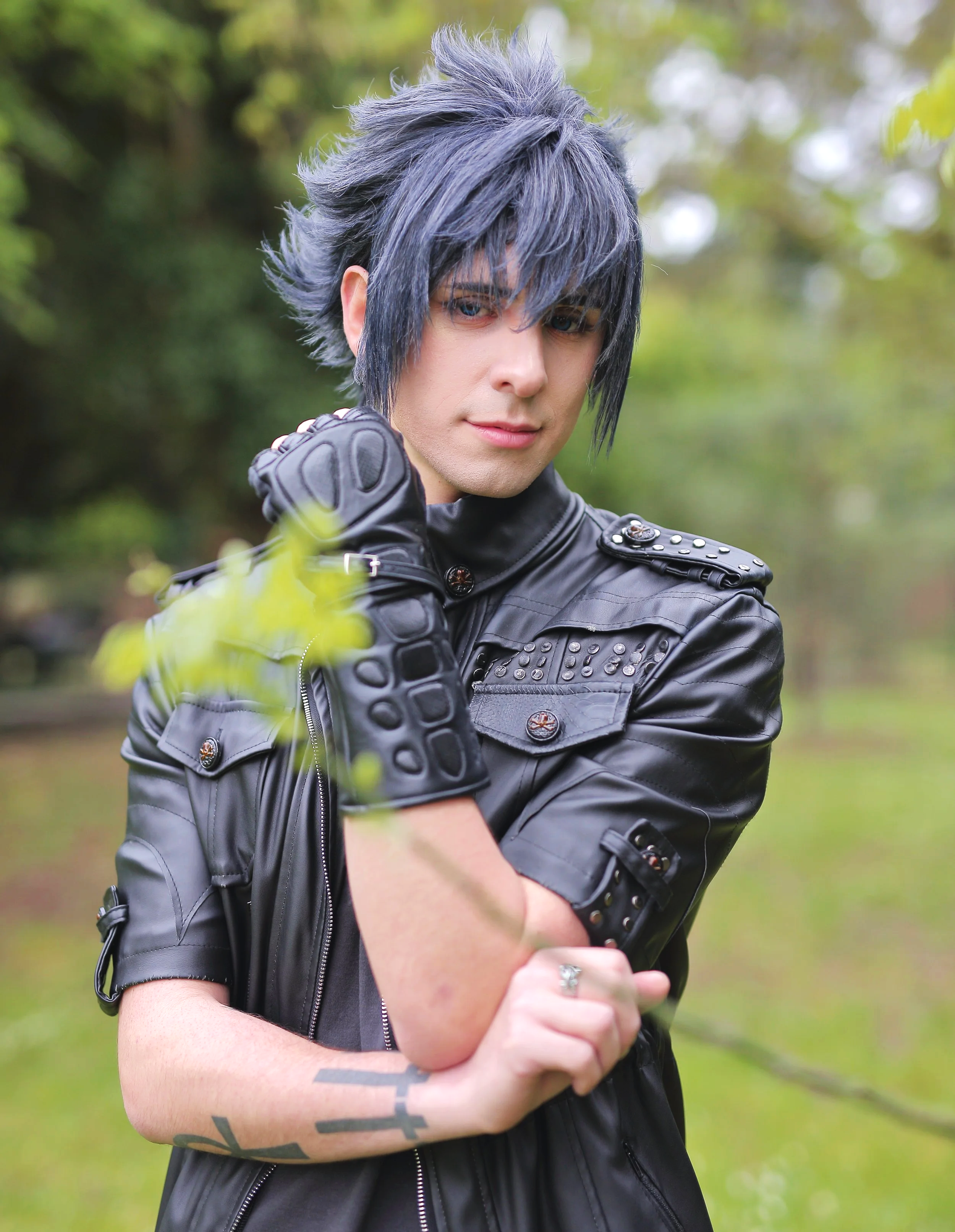 cosplayer au cheveux noirs et gris coiffés portant veste cuir noir posant à l'extérieur parmi les arbres cosplayer cosplay anime manga gaming jeu vidéo personnage déguisement