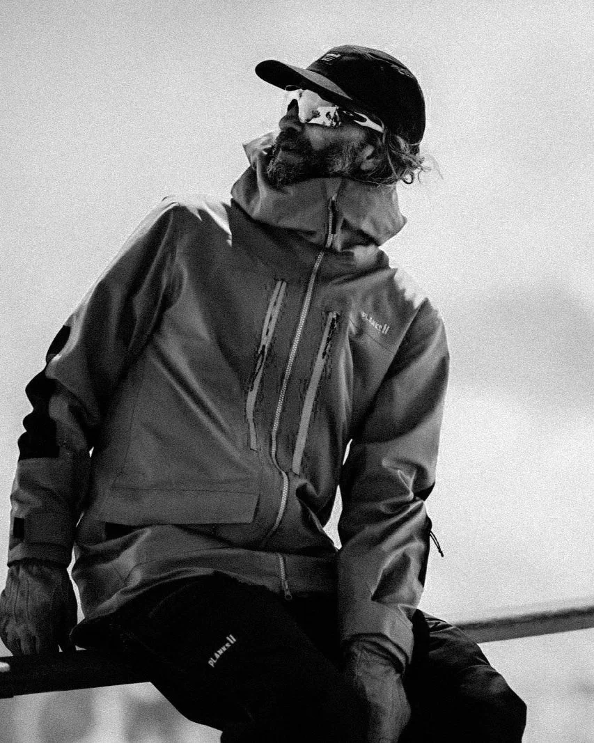 Black and white photo of a man with glasses and a beanie, making a peace sign with his right hand.