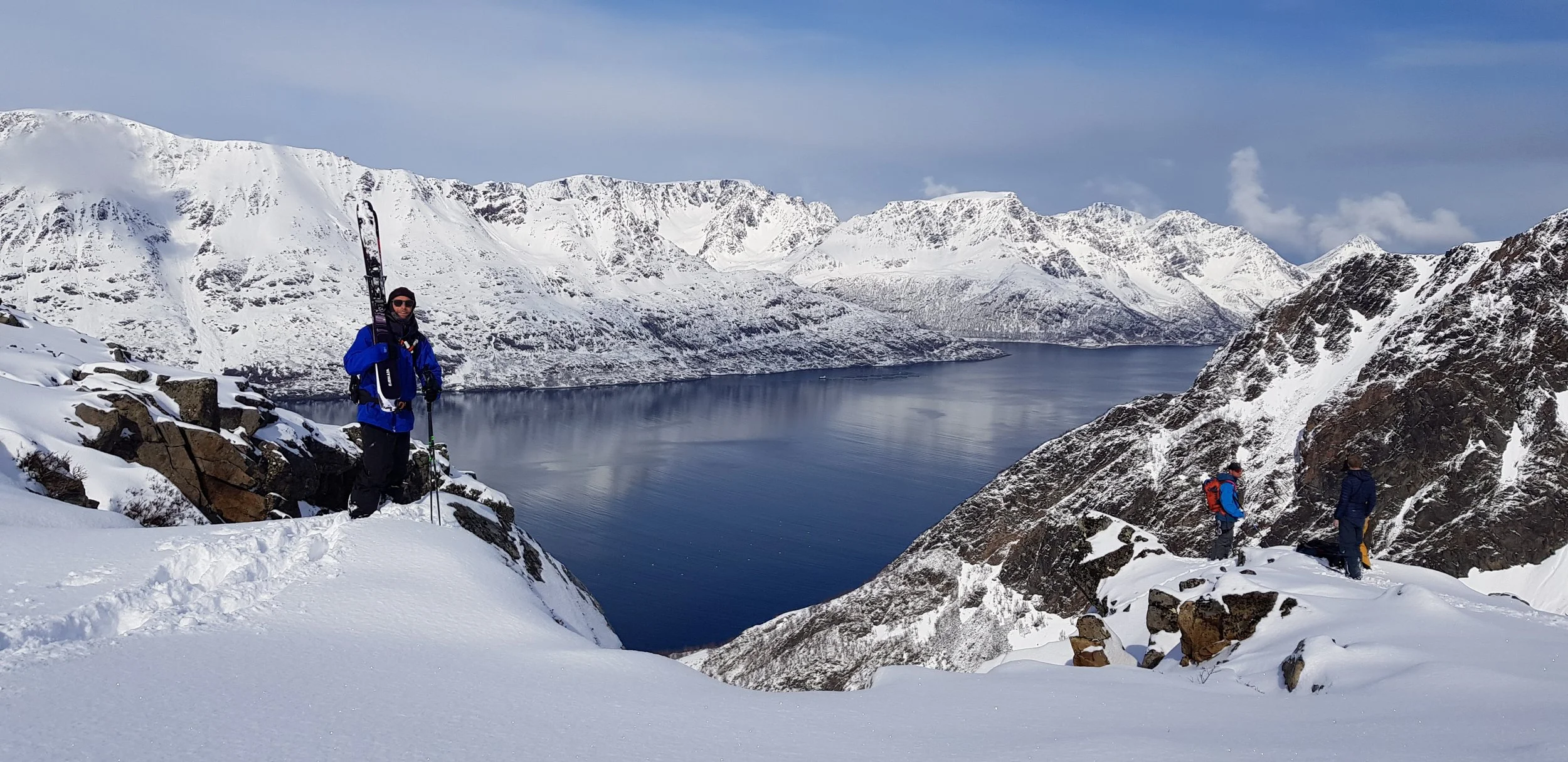 Skier standing on a mountain summit in Norway with a fjord below.