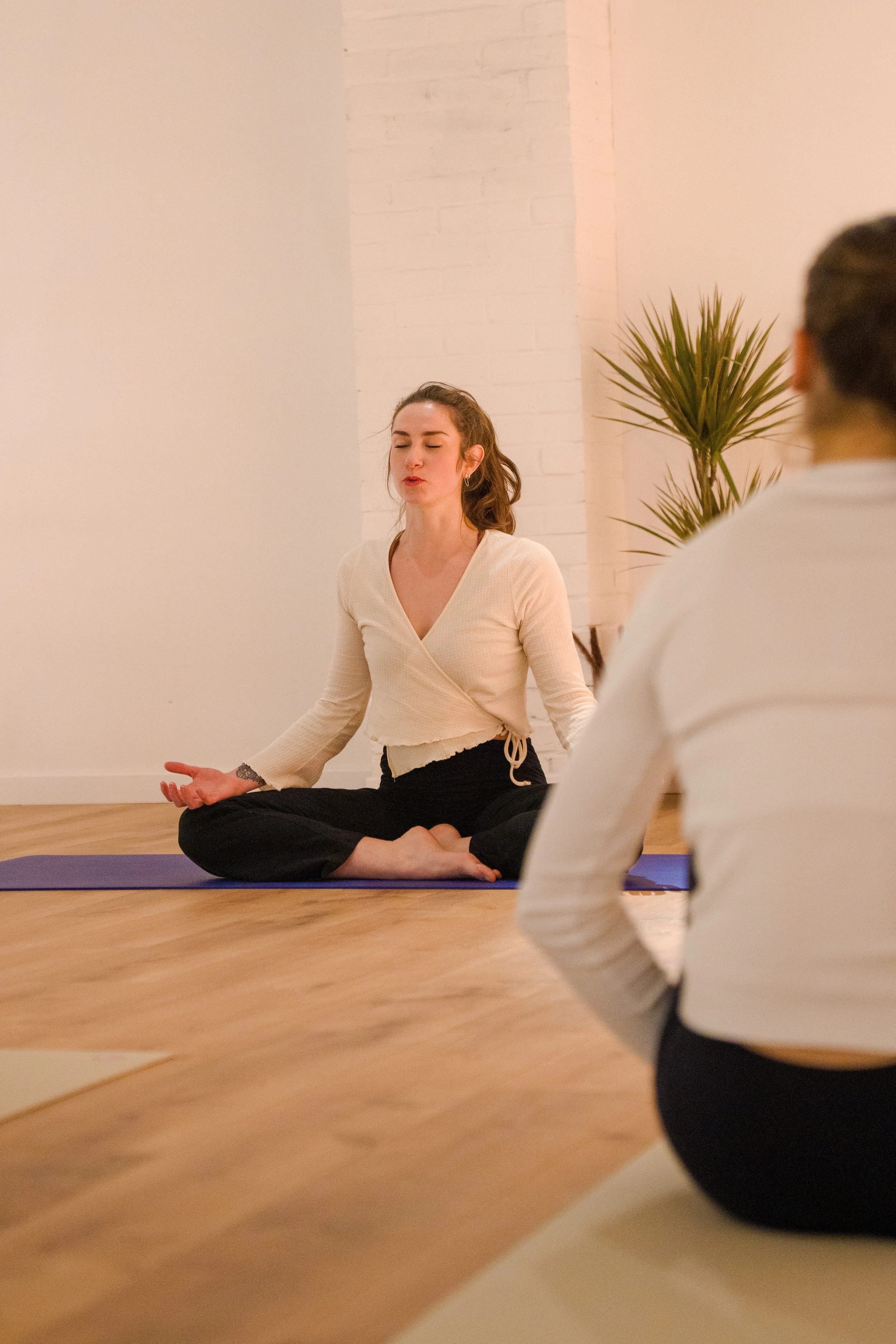 femme assise en tailleur pratiquant le Yoga dans une salle lumineuse