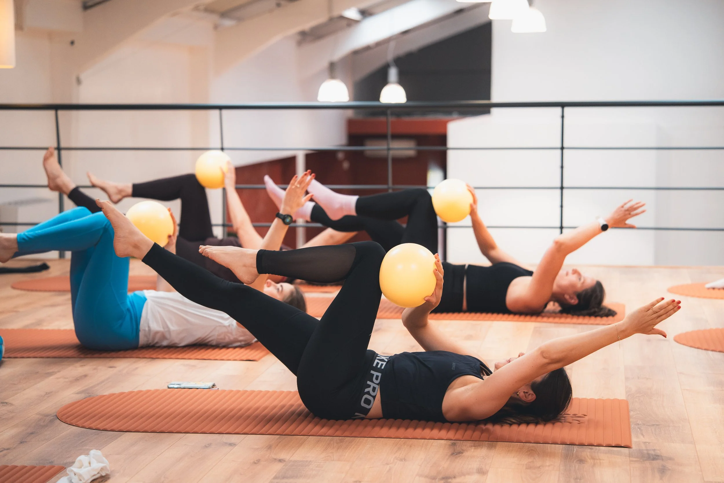 Cours de Pilates avec Ballon, femmes allongée au sol avec ballon jaune dans les mains