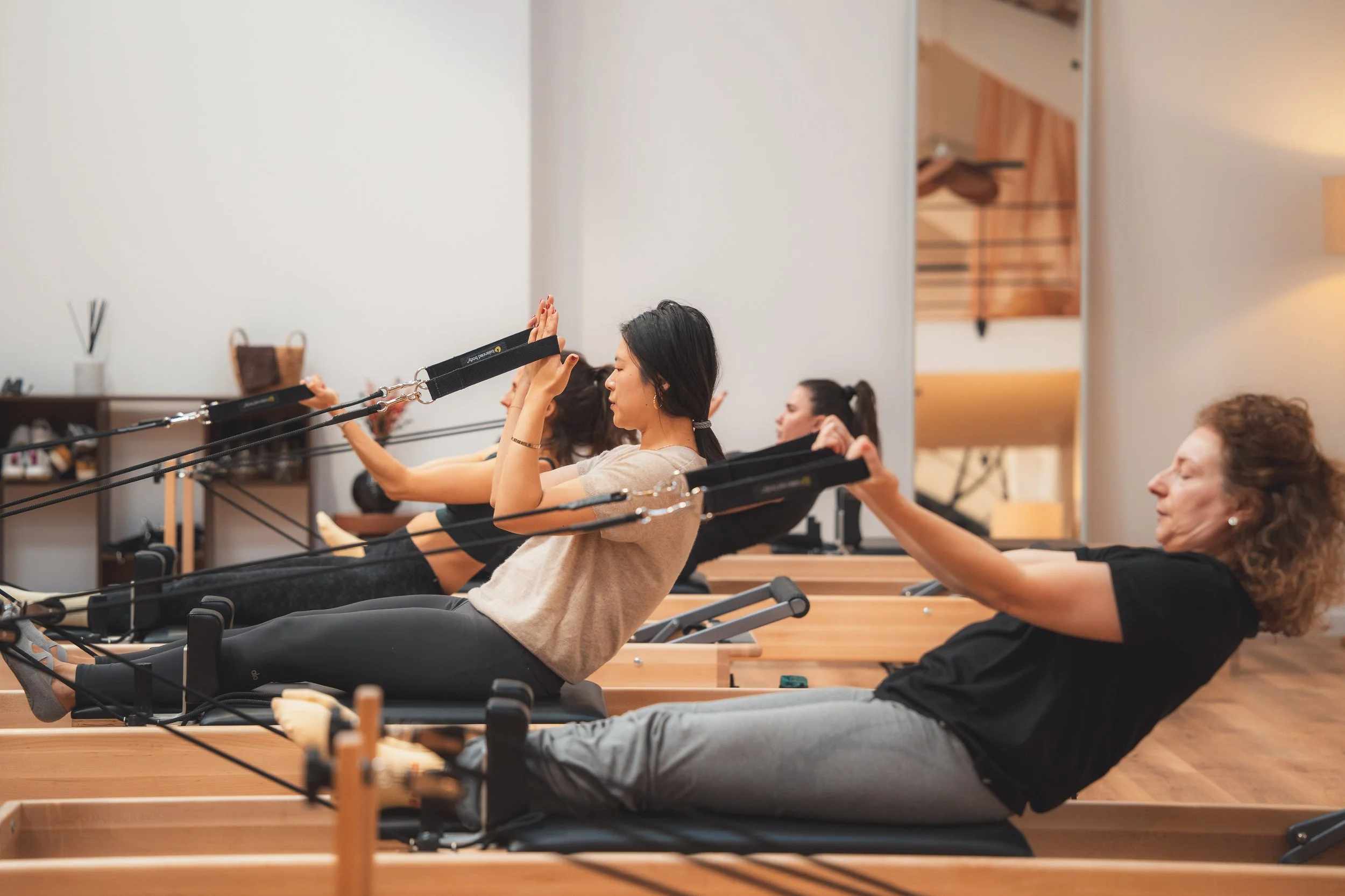 femmes pratiquant le Pilates Reformer au studio Auréa, elles tiennent des sangles sur machine reformer balanced body