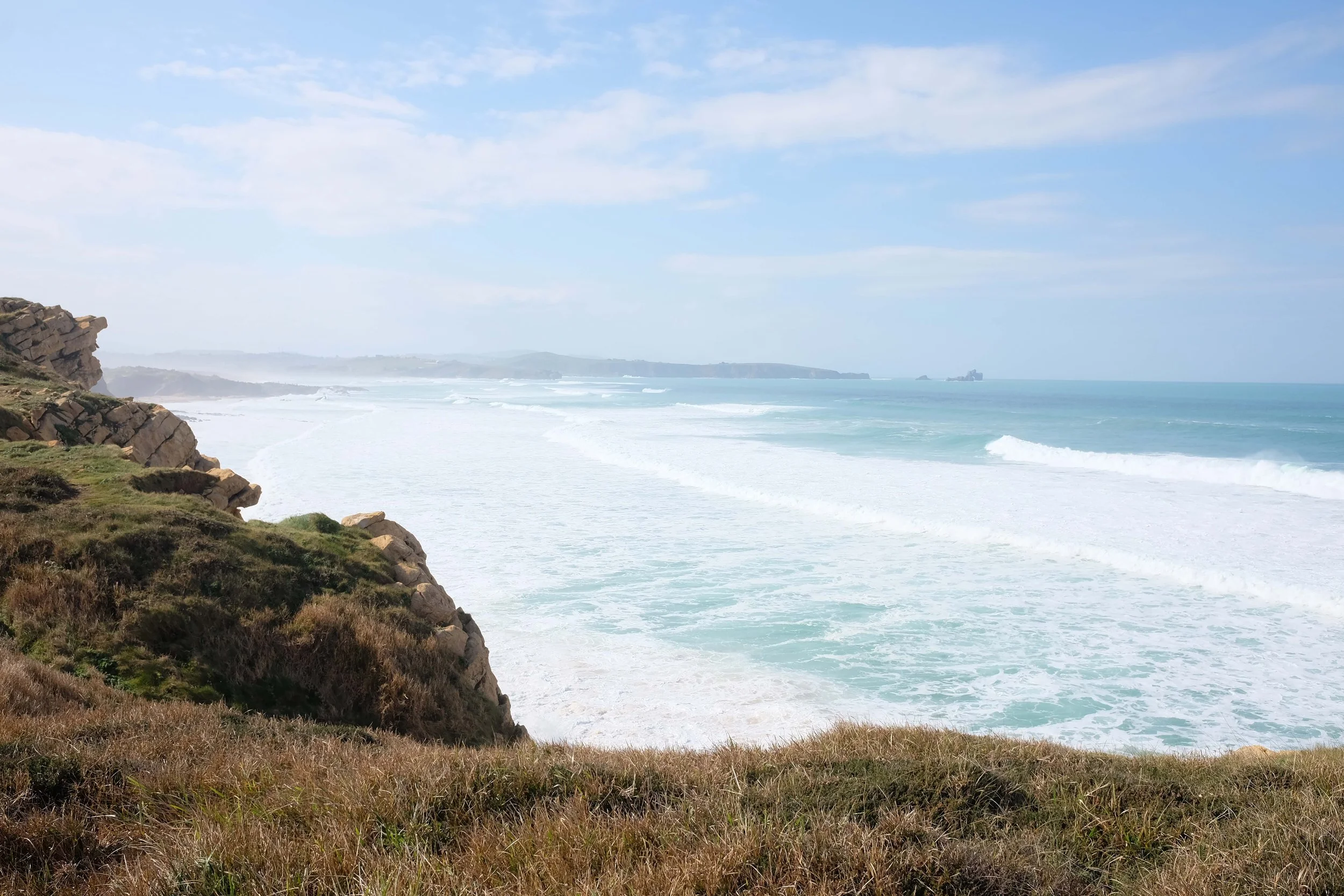 Vista de una costa con acantilados, hierba y el mar con olas.