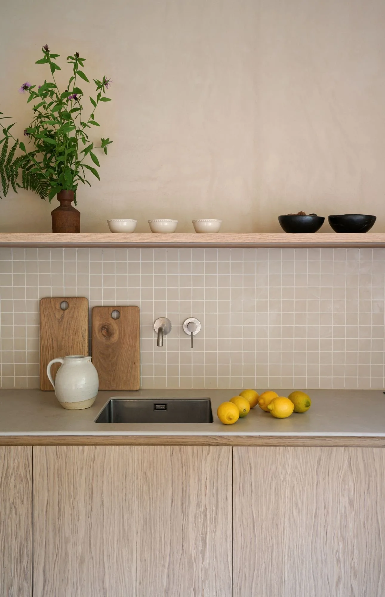 View of a modern kitchen with wooden countertop, stainless steel sink, lemons on the table and kitchen utensils, including wooden cutting boards and vase with plants.