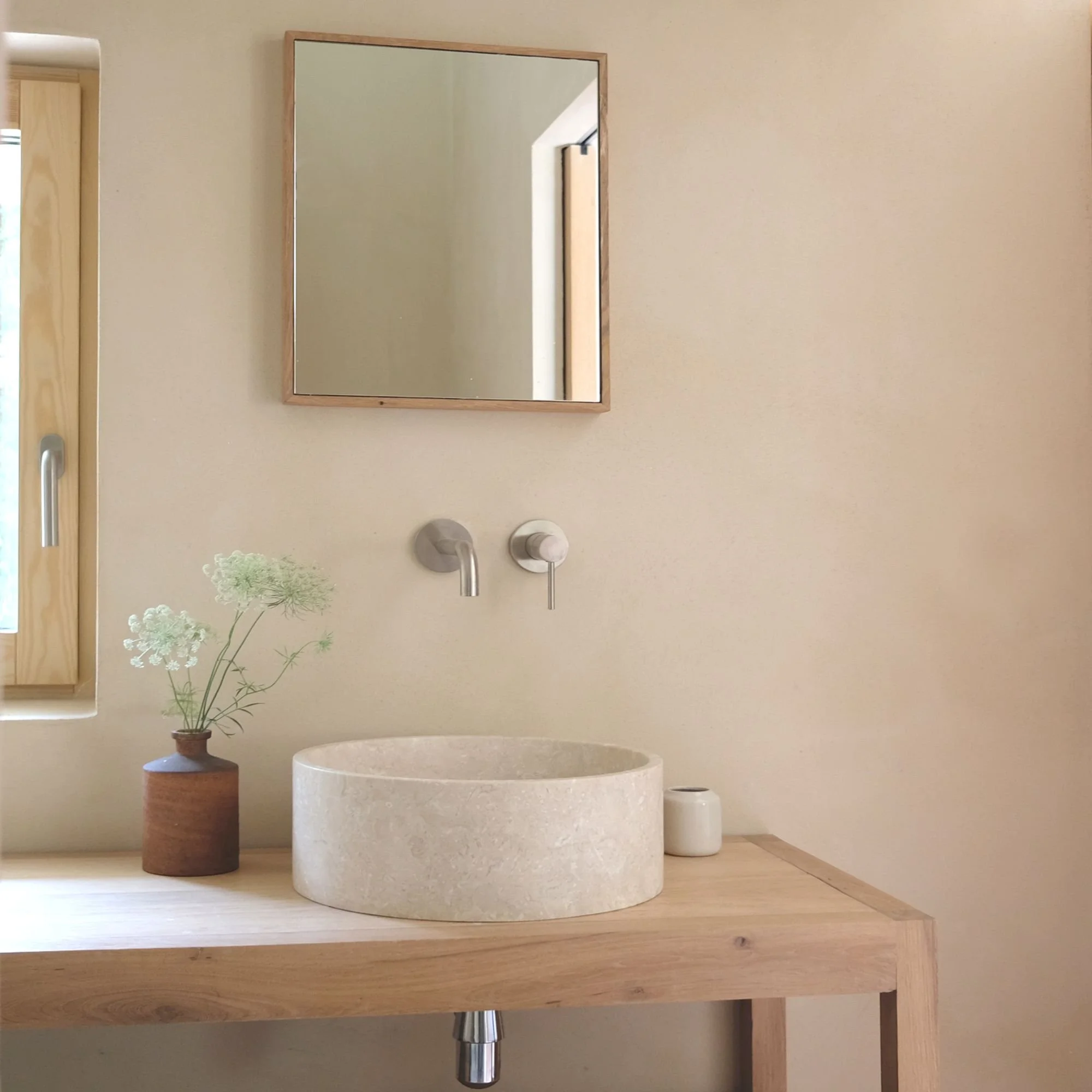 Lavabo de piedra sobre un mueble de madera con una planta en un jarrón, un vaso y un espejo sobre la pared
