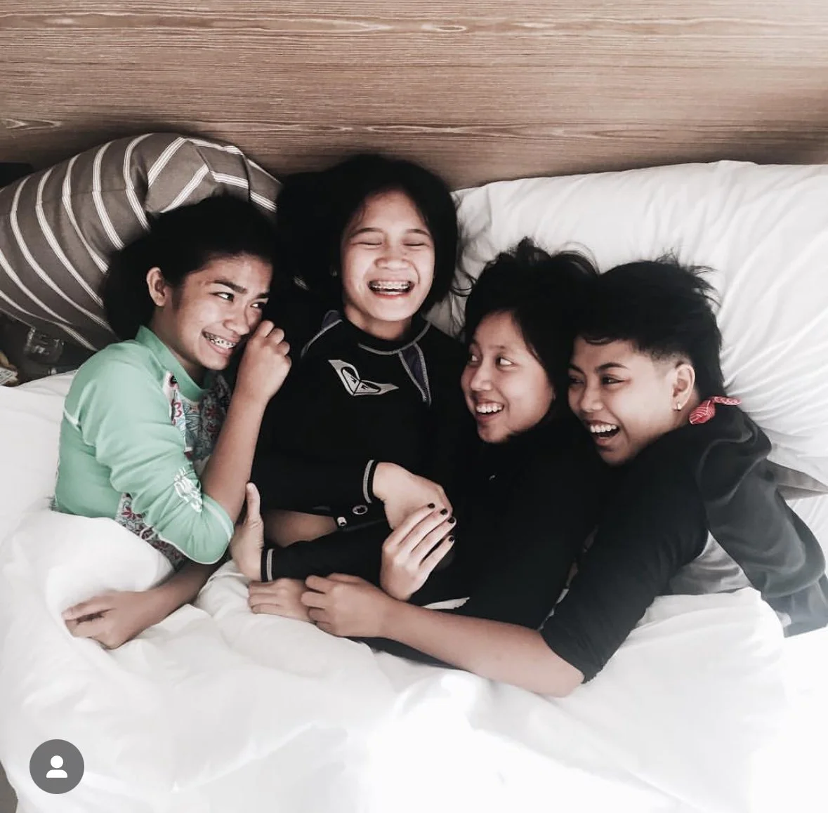Four children are playing and laughing together on a bed.