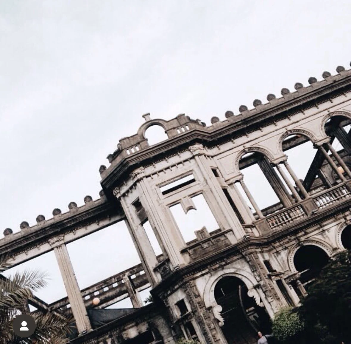 Dilapidated, multi-story, neoclassical building with broken windows and arches, showing signs of decay, under an overcast sky.