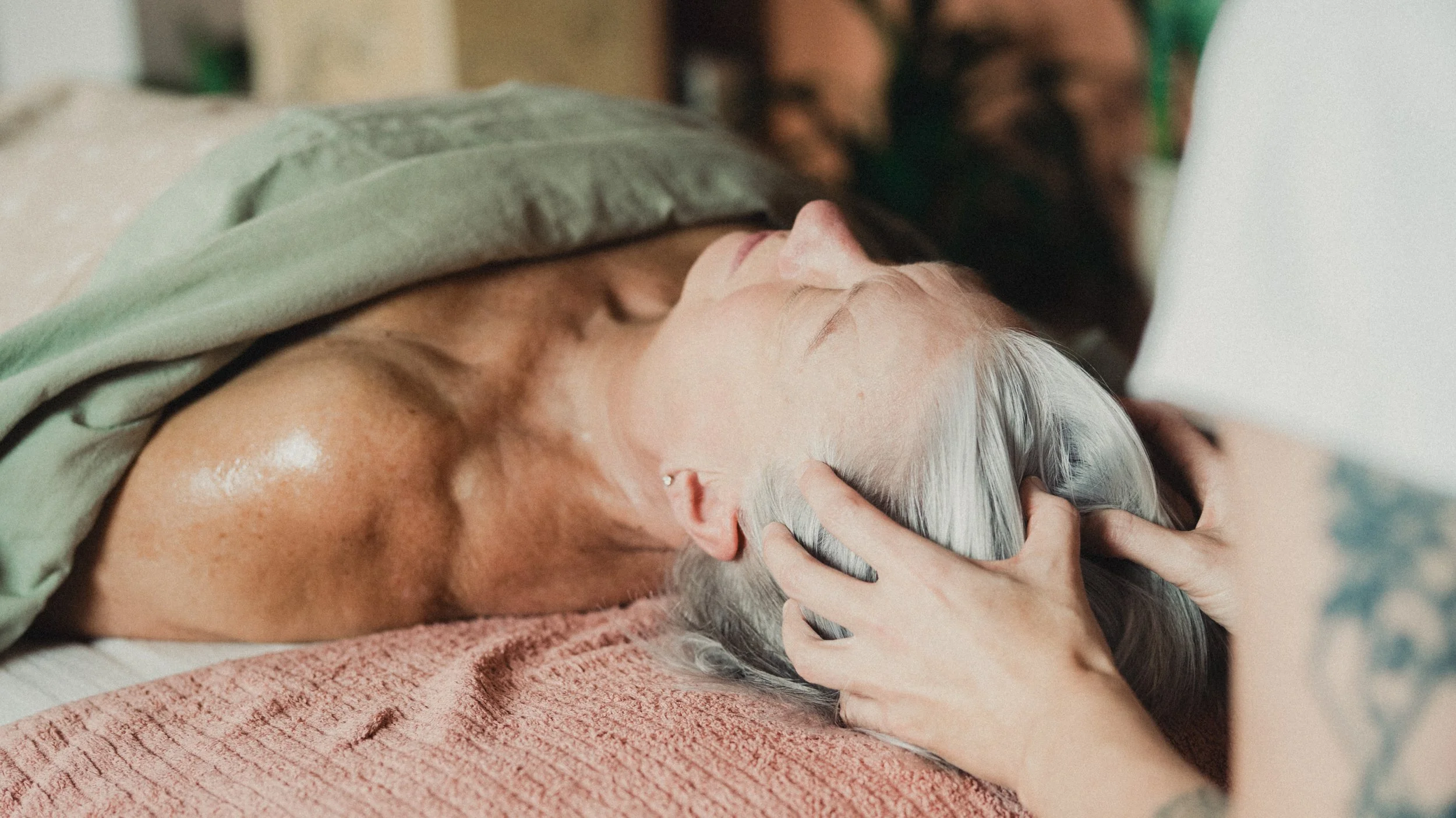 Elderly woman resting in bed while a caregiver gently cradles her head.