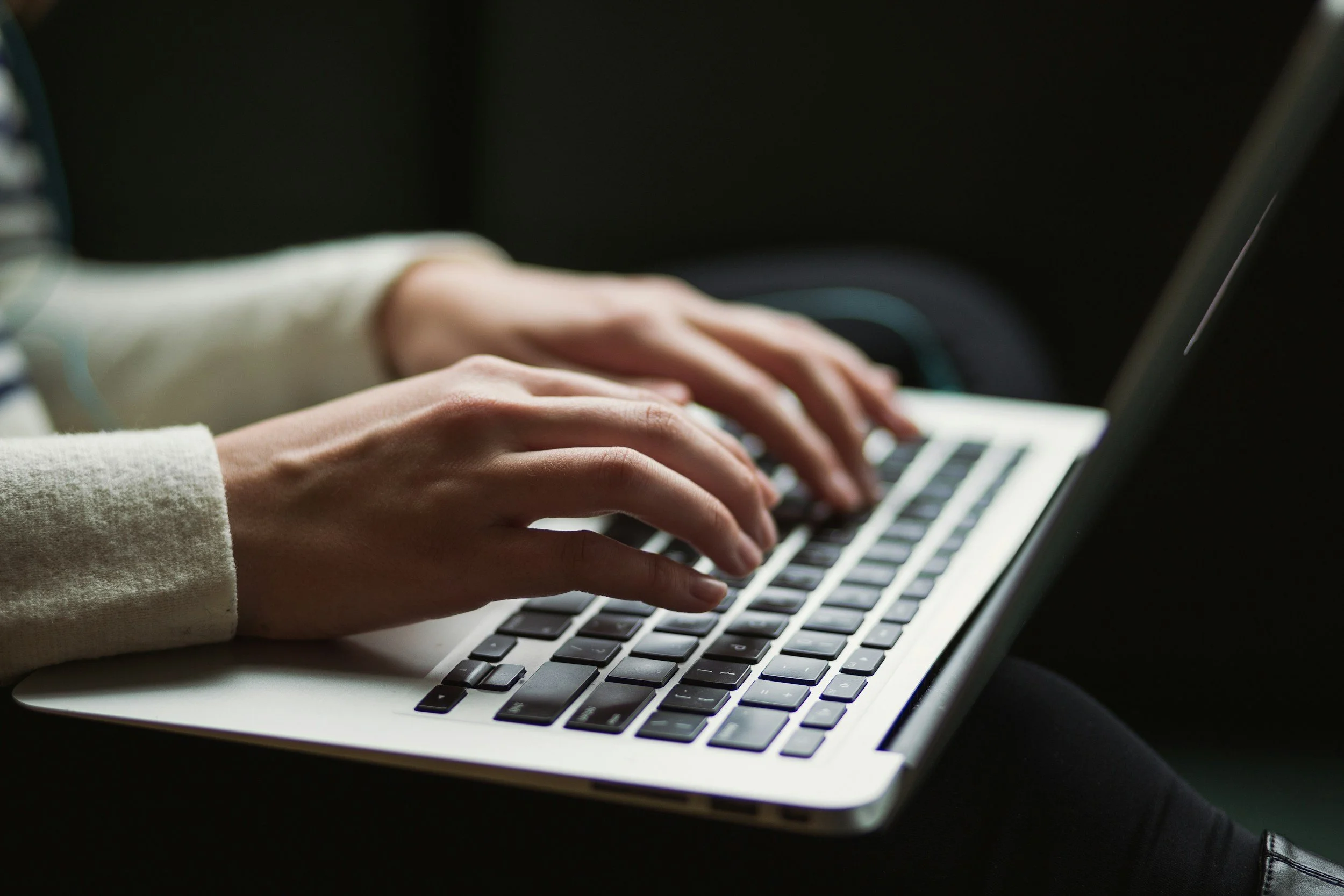 Person typing on a laptop keyboard with dark background.
