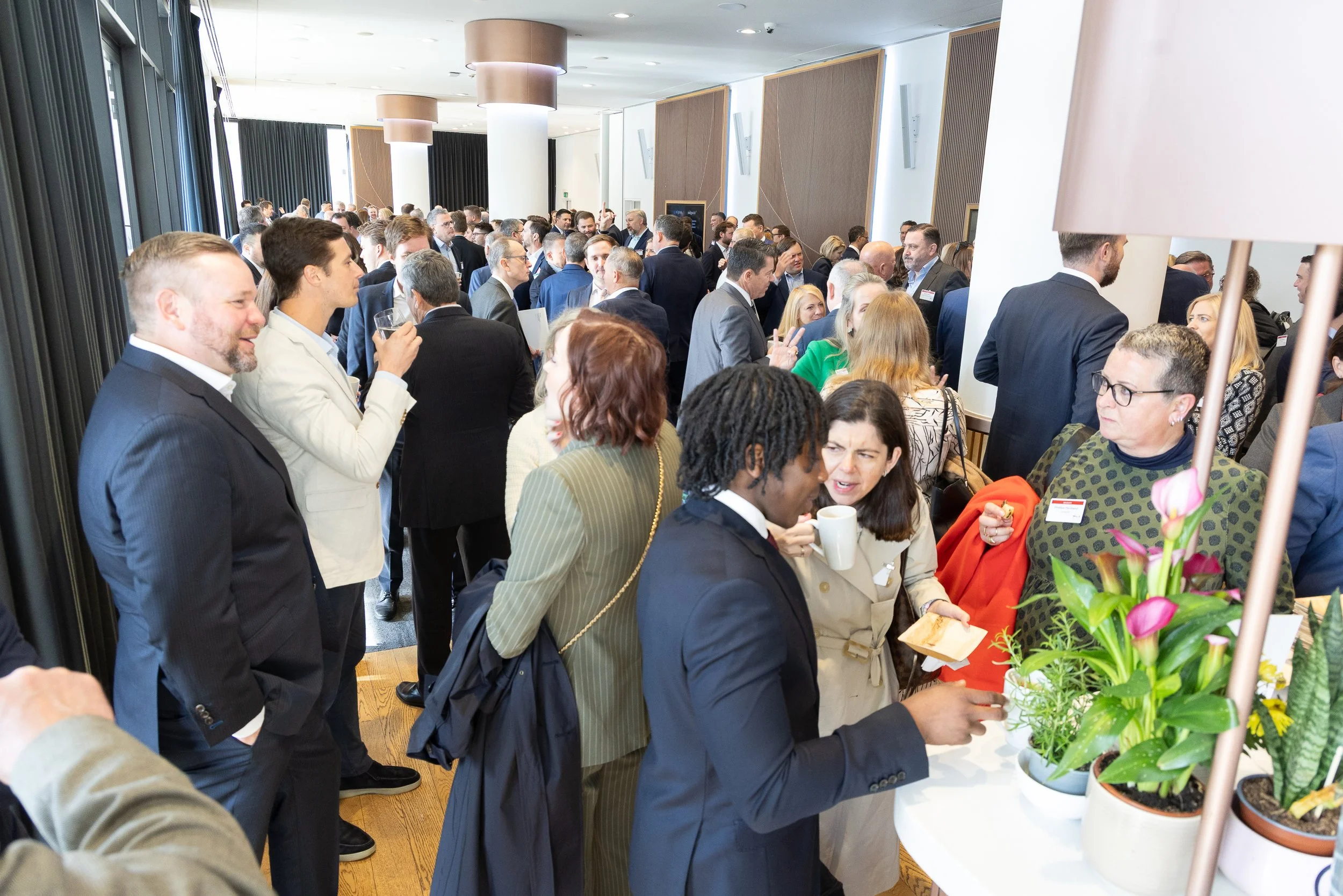 Crowd of people socializing at a professional event or conference in a spacious, well-lit room with modern decor.