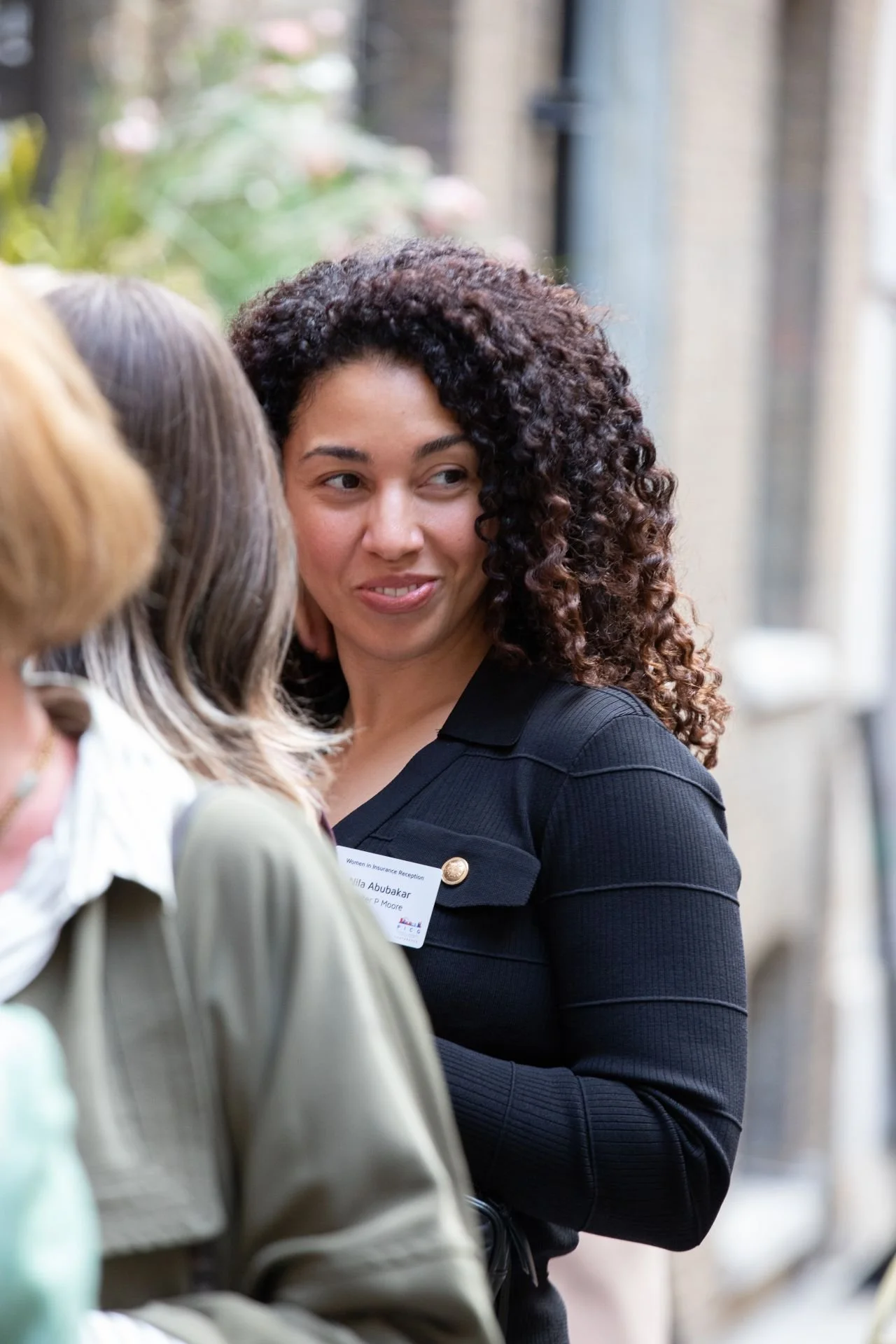 A woman with curly hair and a black top engaging in conversation at an outdoor event.