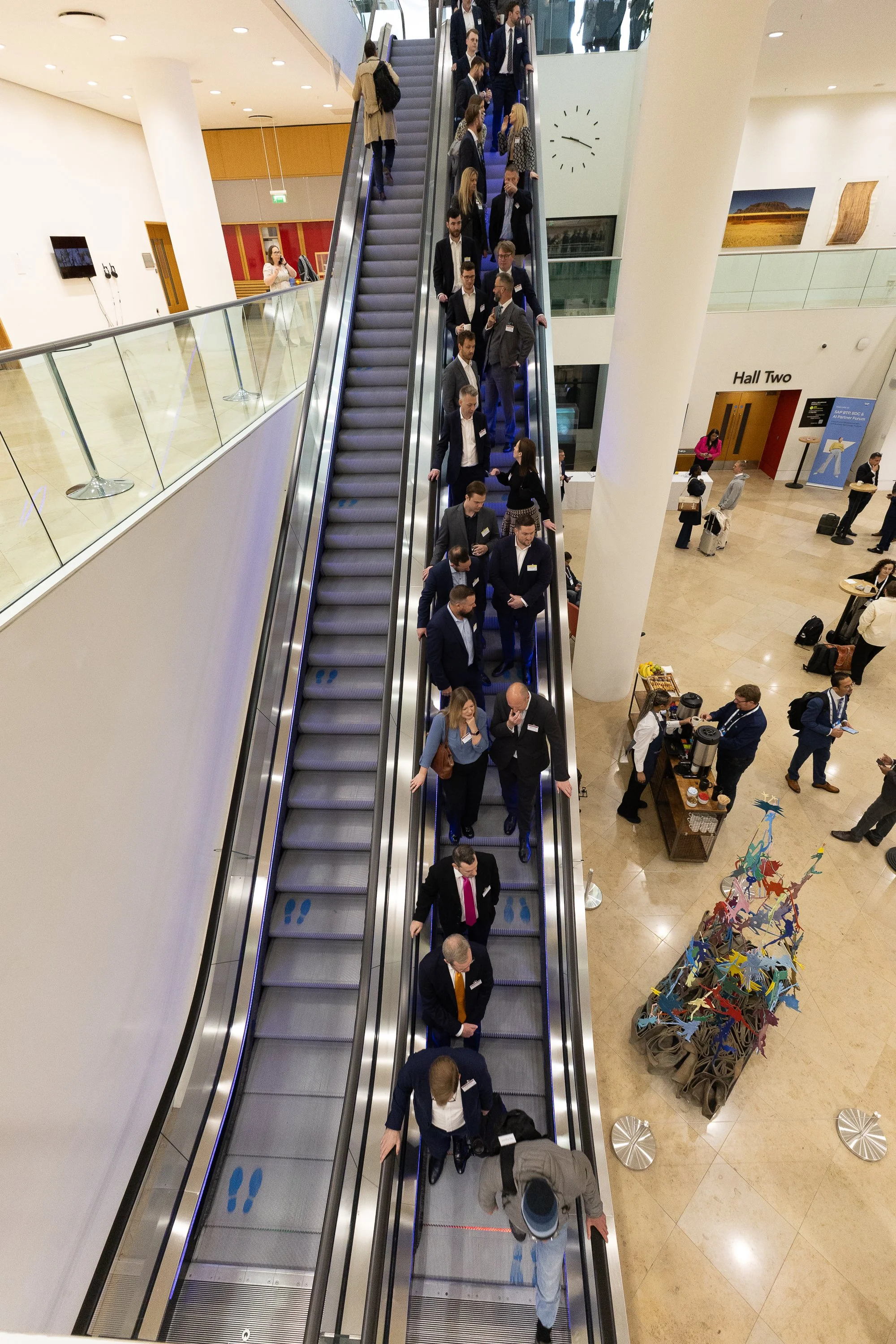 A group of business professionals riding an escalator in a modern conference center or airport.