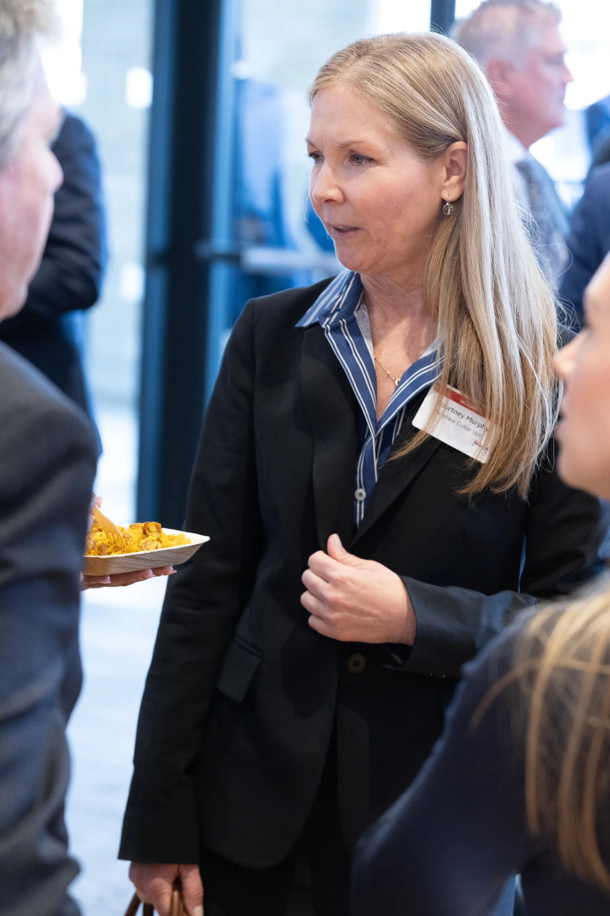 Businesswoman engaging in conversation at a networking event, holding a plate of food.