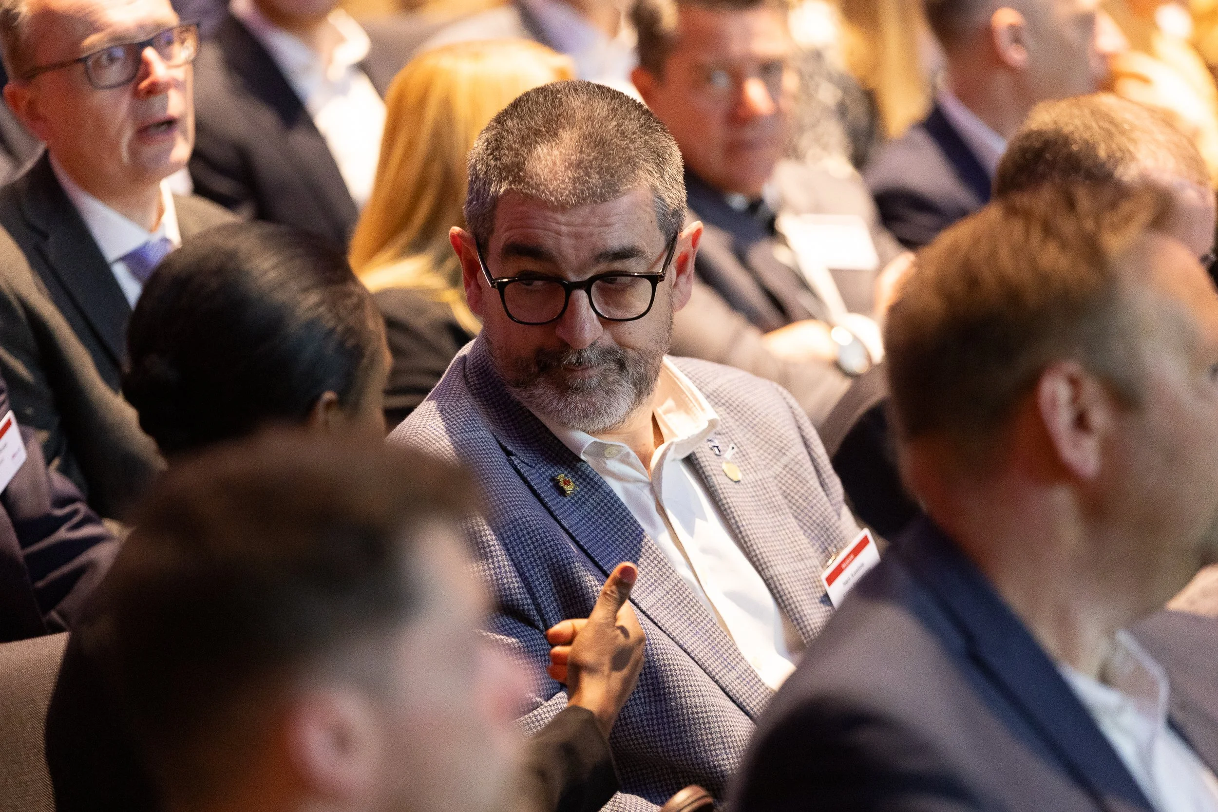 A diverse group of business professionals attending a conference, sitting in an auditorium, with some taking notes or listening attentively.