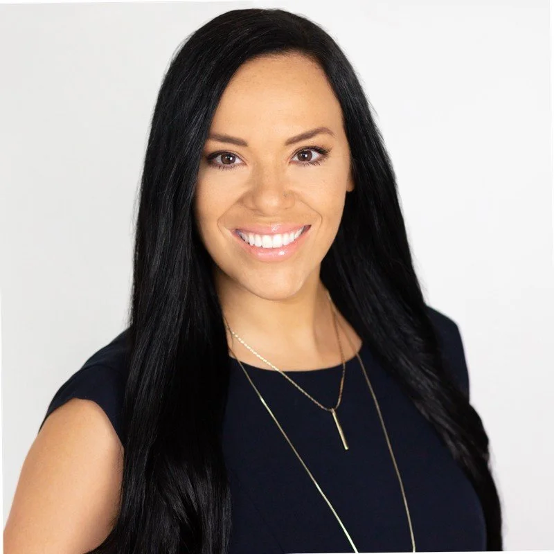 A man with dark, curly hair, glasses, and a beard looking to the side in a well-lit room.