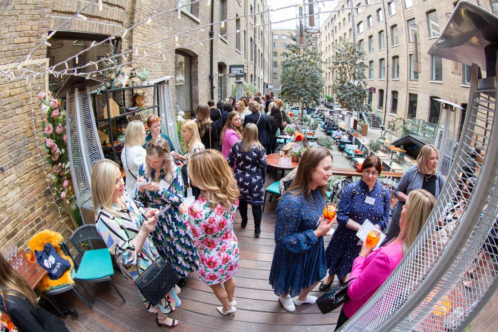 People socializing on a rooftop patio, some holding drinks, with seating and outdoor decor.