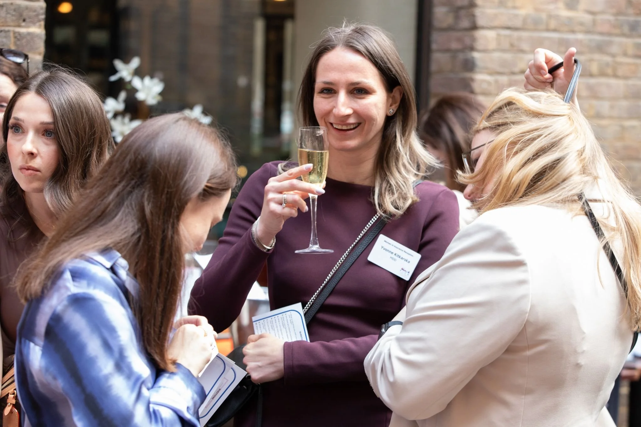 Group of women at a networking event, one woman holding a glass of champagne and smiling.