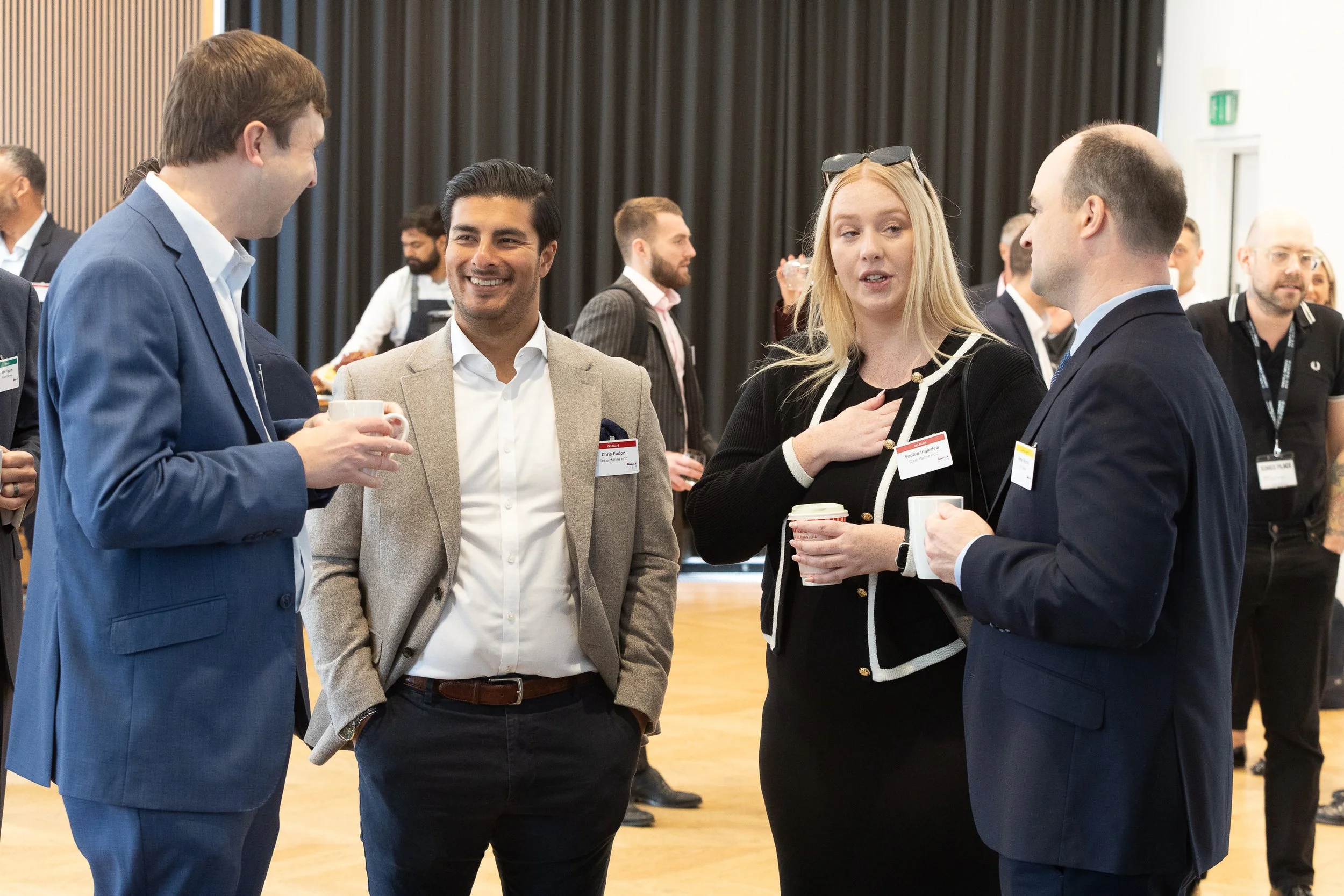Business professionals at a networking event having a conversation, holding coffee cups.