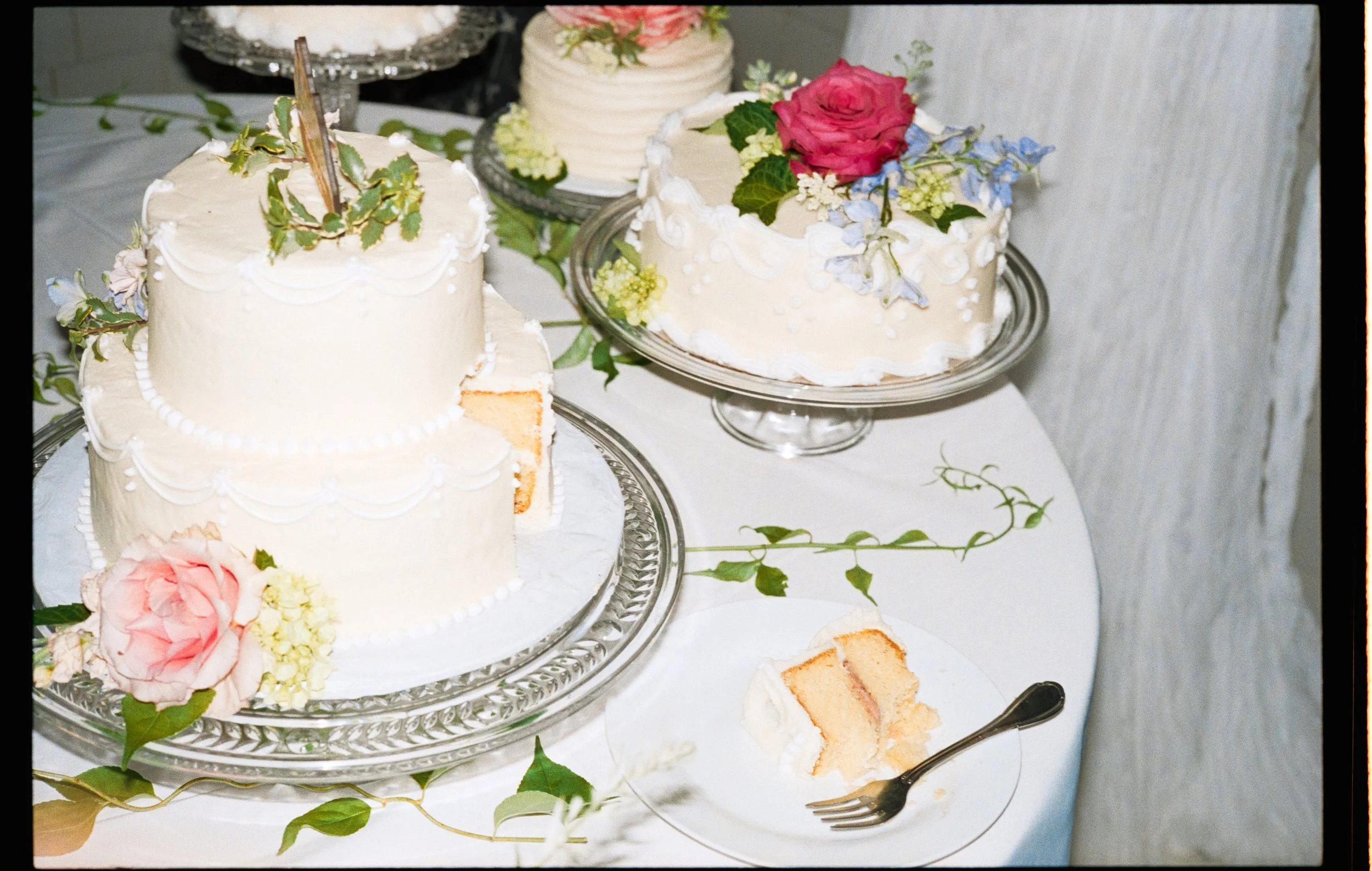 A two teird wedding cake decorated with real roses has been cut and the first slice is partly eaten, left on the table.