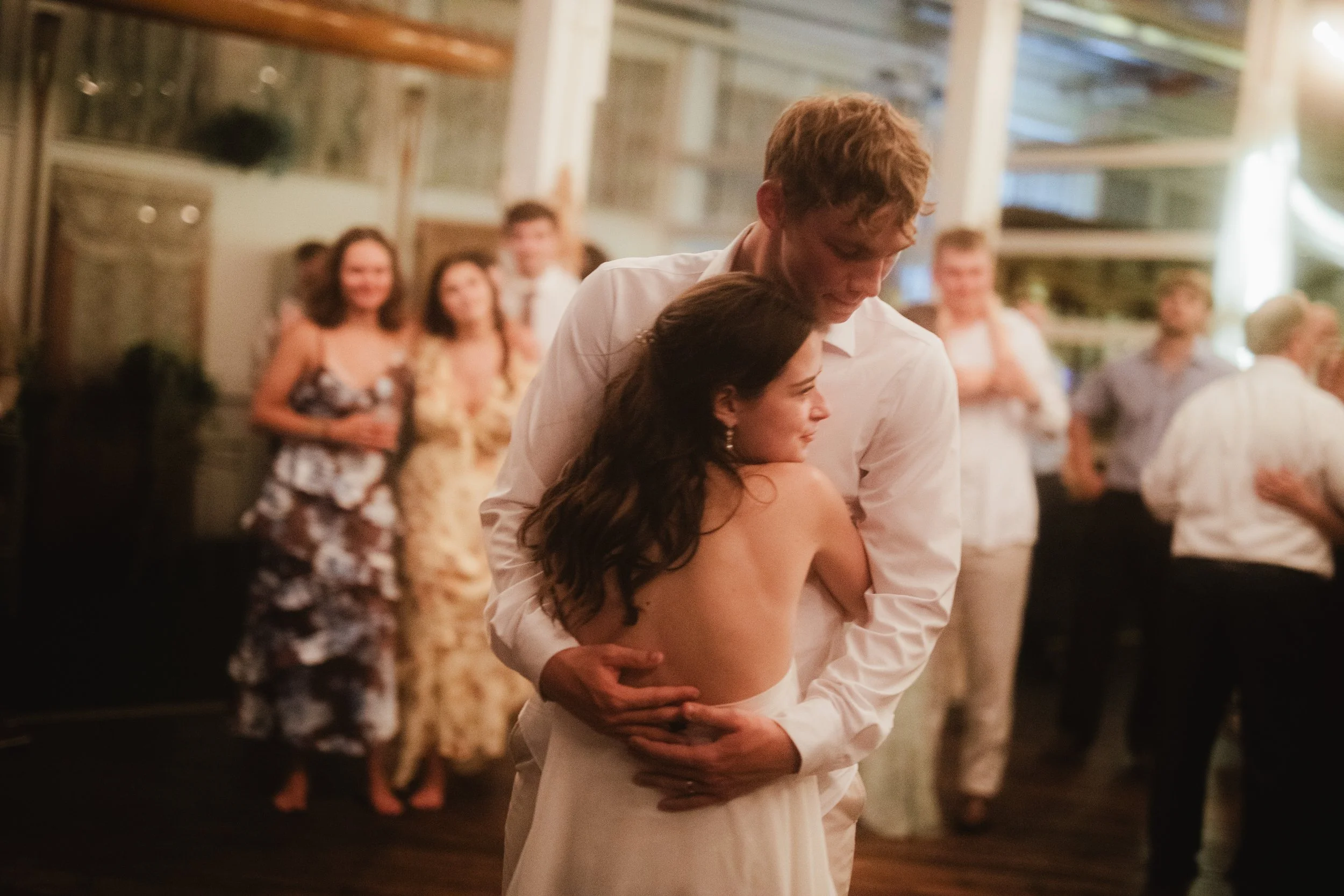 A couple embraces on the dance floor while guest observe from off the dance floor.