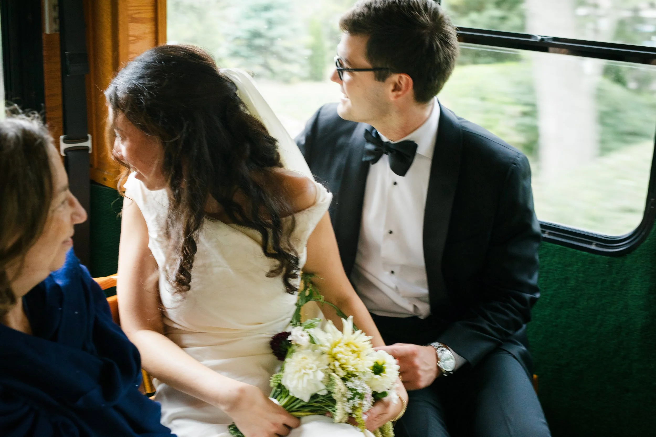 On the trolly ride to the wedding ceremony the couple looks out the back window, the bride to be is holding a bouquet of flowers.