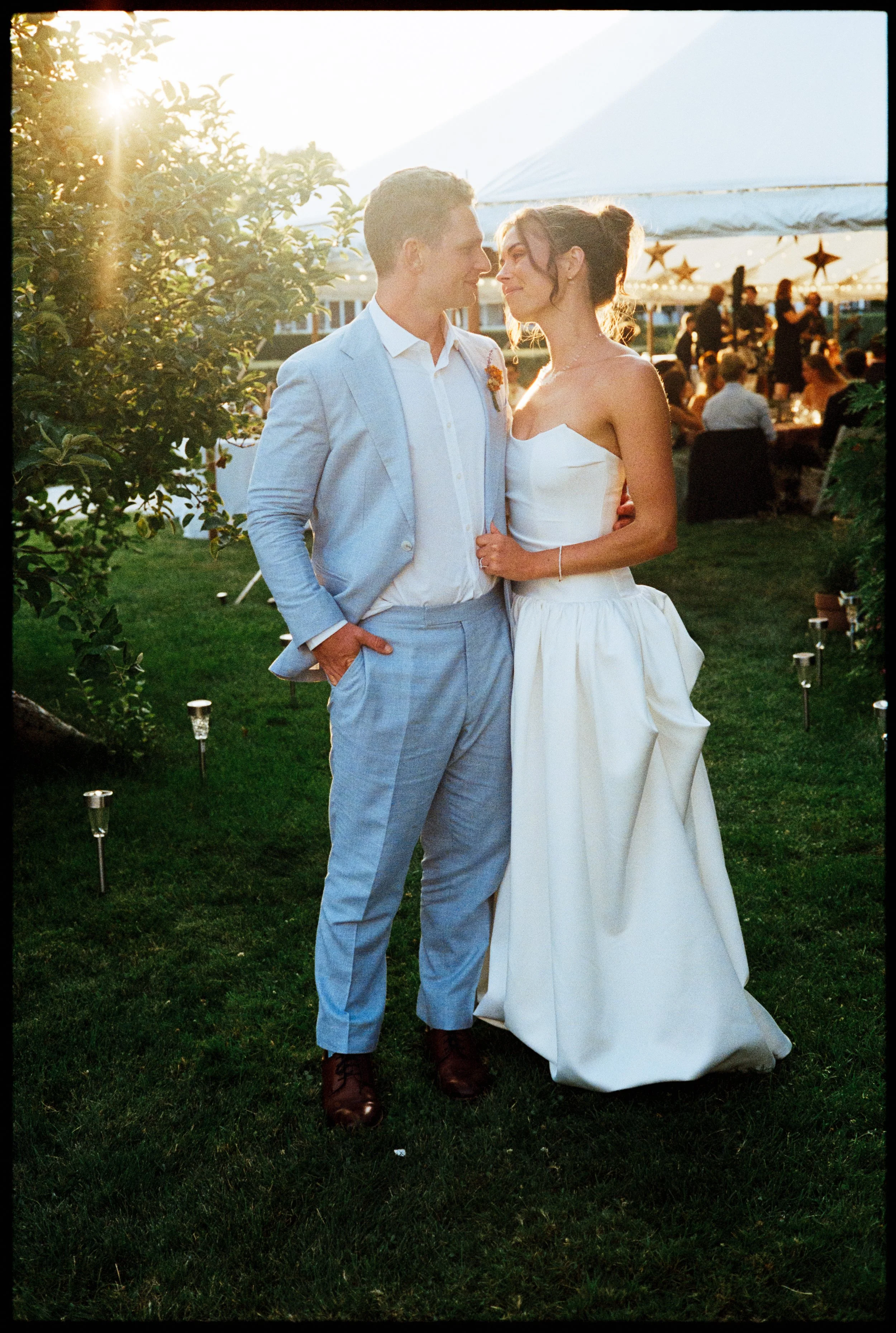 The sun is setting as this couple gazes lovingly into one another's eyes. They are surrounded by the celebration of their wedding, a tent decorated with paper stars and beautiful crowds.